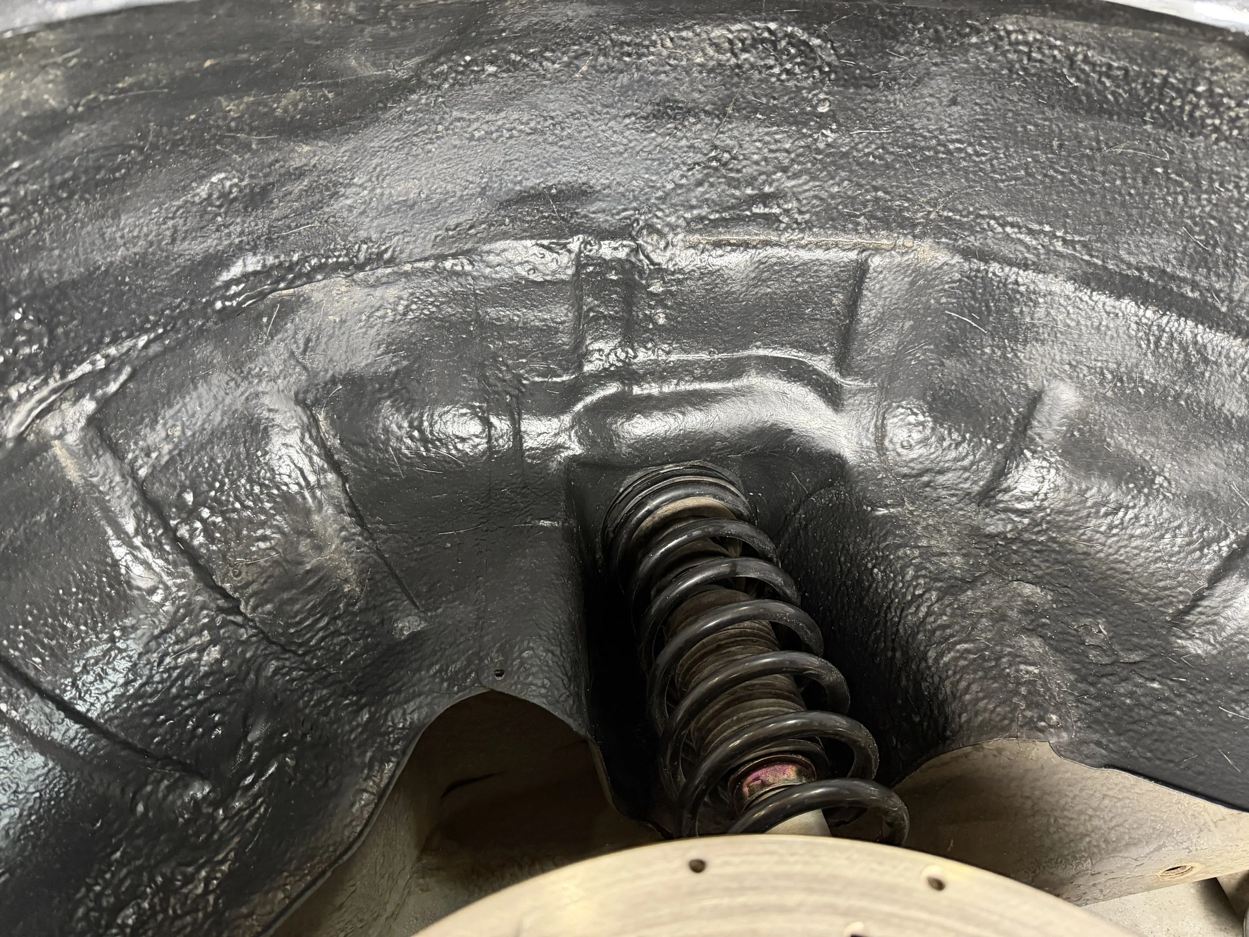 Close-up of a vehicle suspension system showing a coil spring and a black metal component with textured surface.