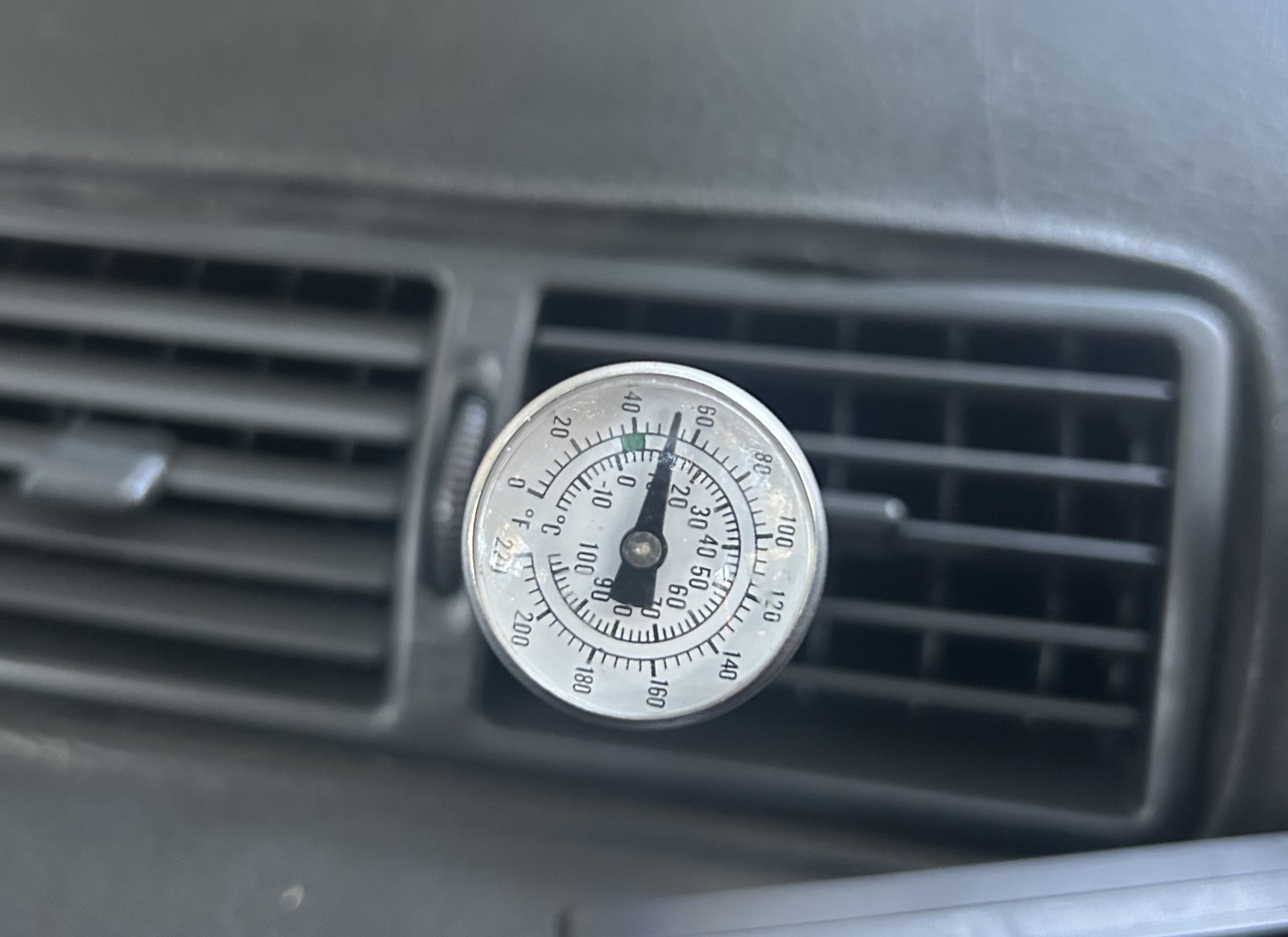 Car air vent with a round thermometer or hygrometer attached, showing temperature and humidity readings.