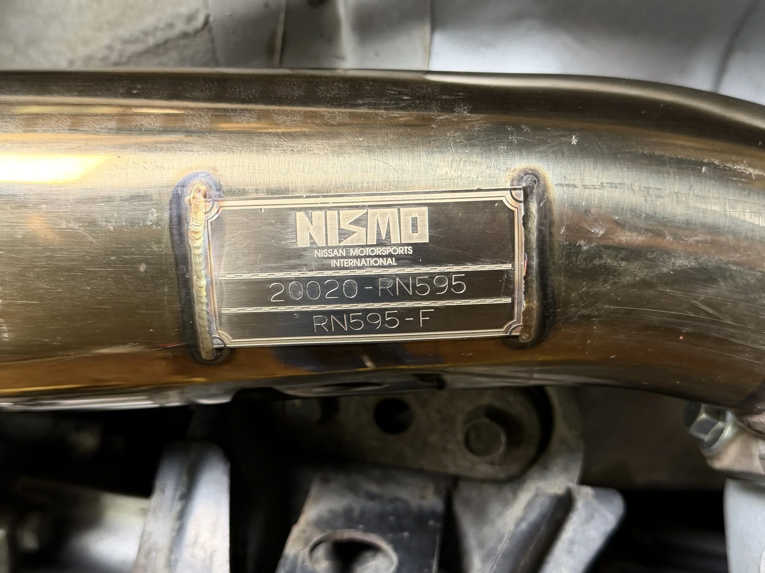 Close-up of a metal plate on a Nissan Motorsports International component, displaying the part number 20020-RN595.