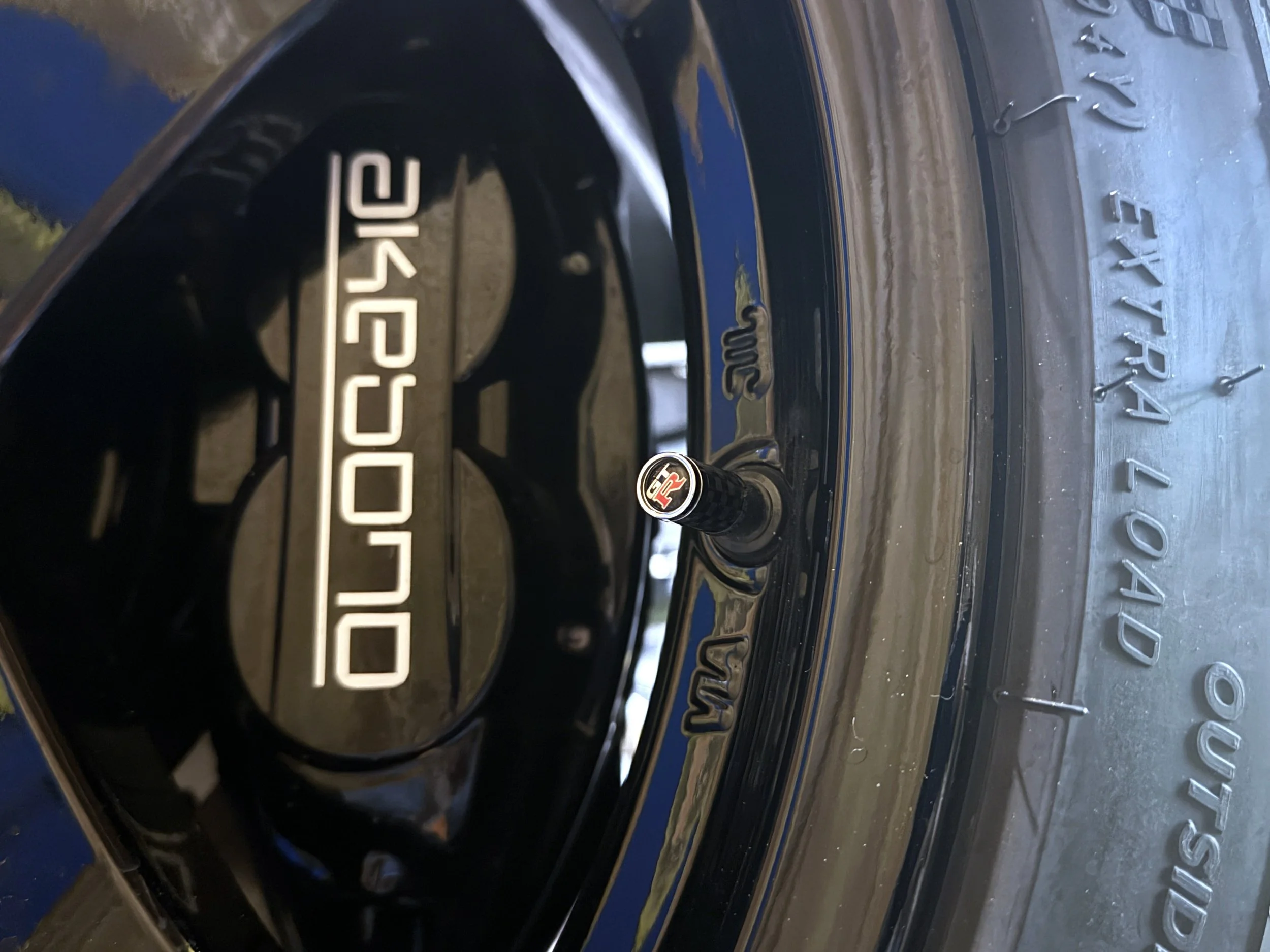 Close-up of a black car wheel with a silver logo that says 'TOYOTA' and a tire. The background includes a textured surface with the text 'TOYOTA' embossed on it.