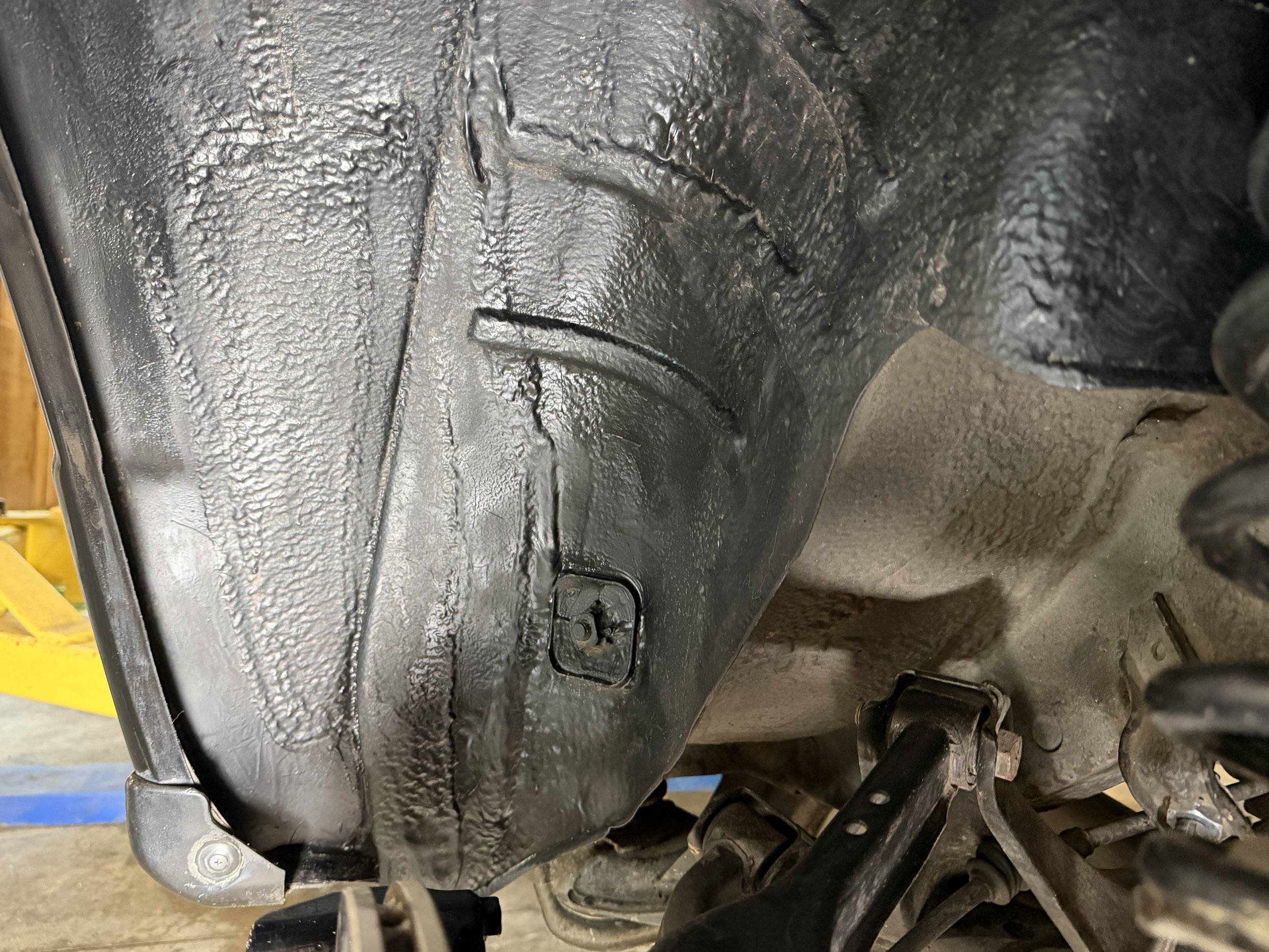 Underneath view of a vehicle's undercarriage with black coating and visible suspension components.