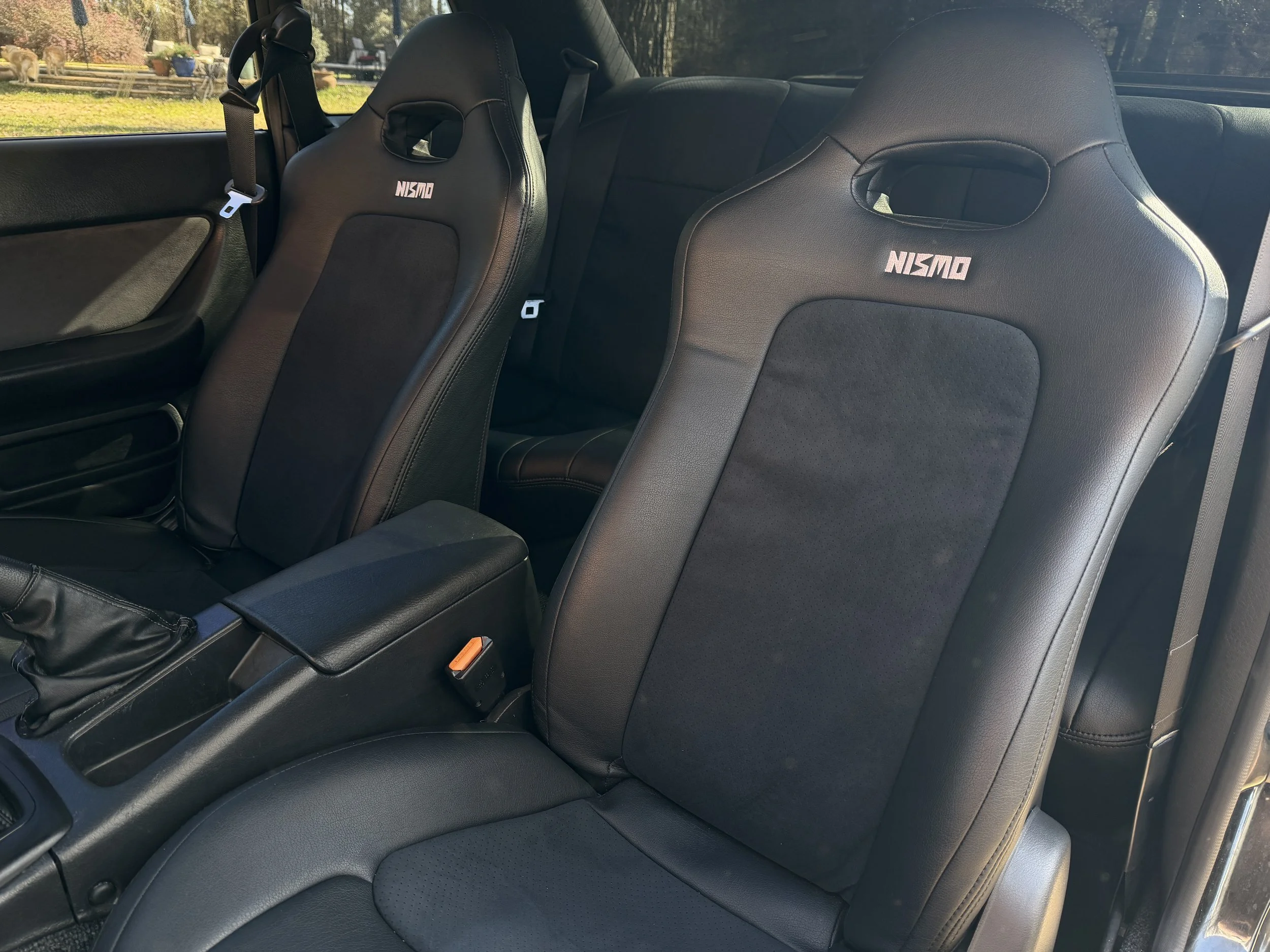 The interior of a car showing two black racing style seats with the "NISMO" logo, next to a center console and door panel.