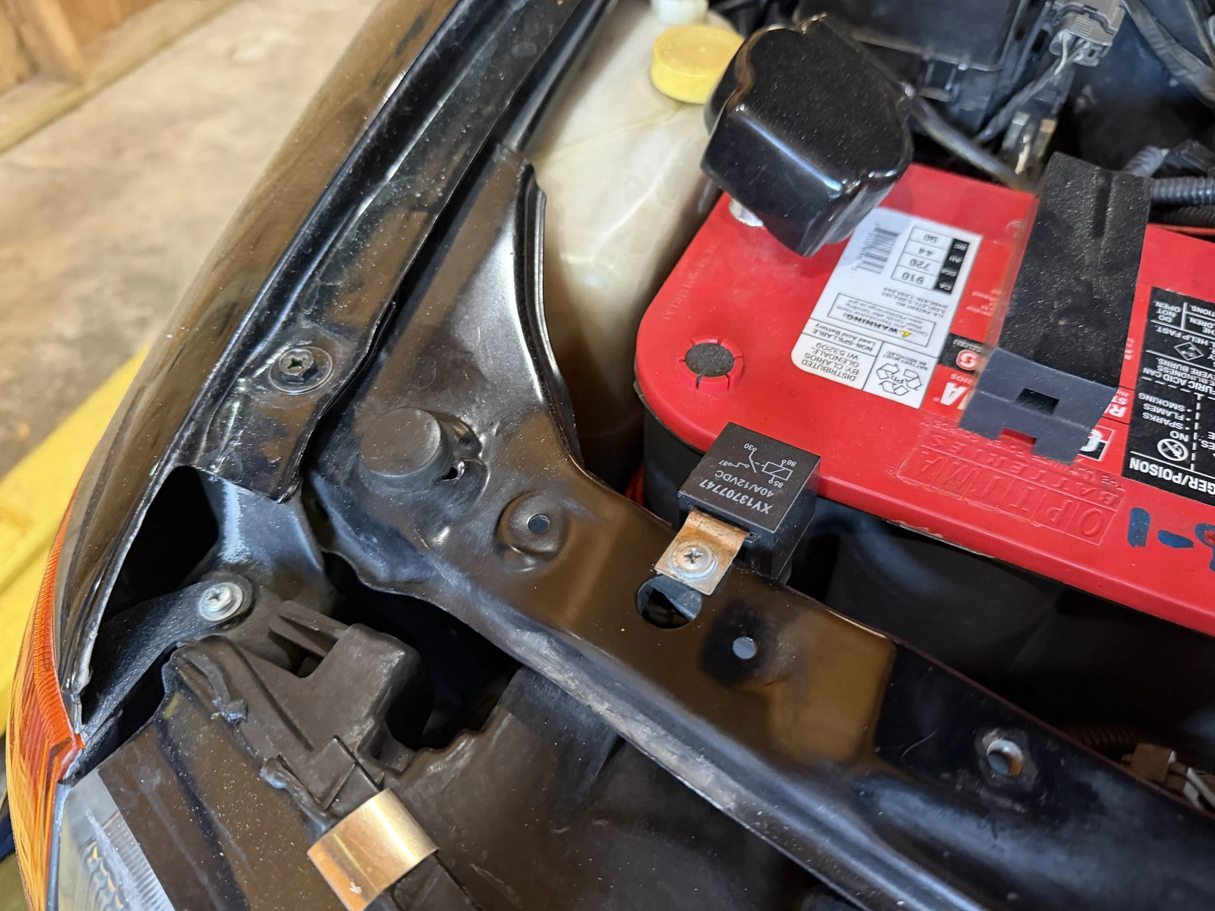Close-up of a car engine bay with a red car battery, a black relay, and various engine components.