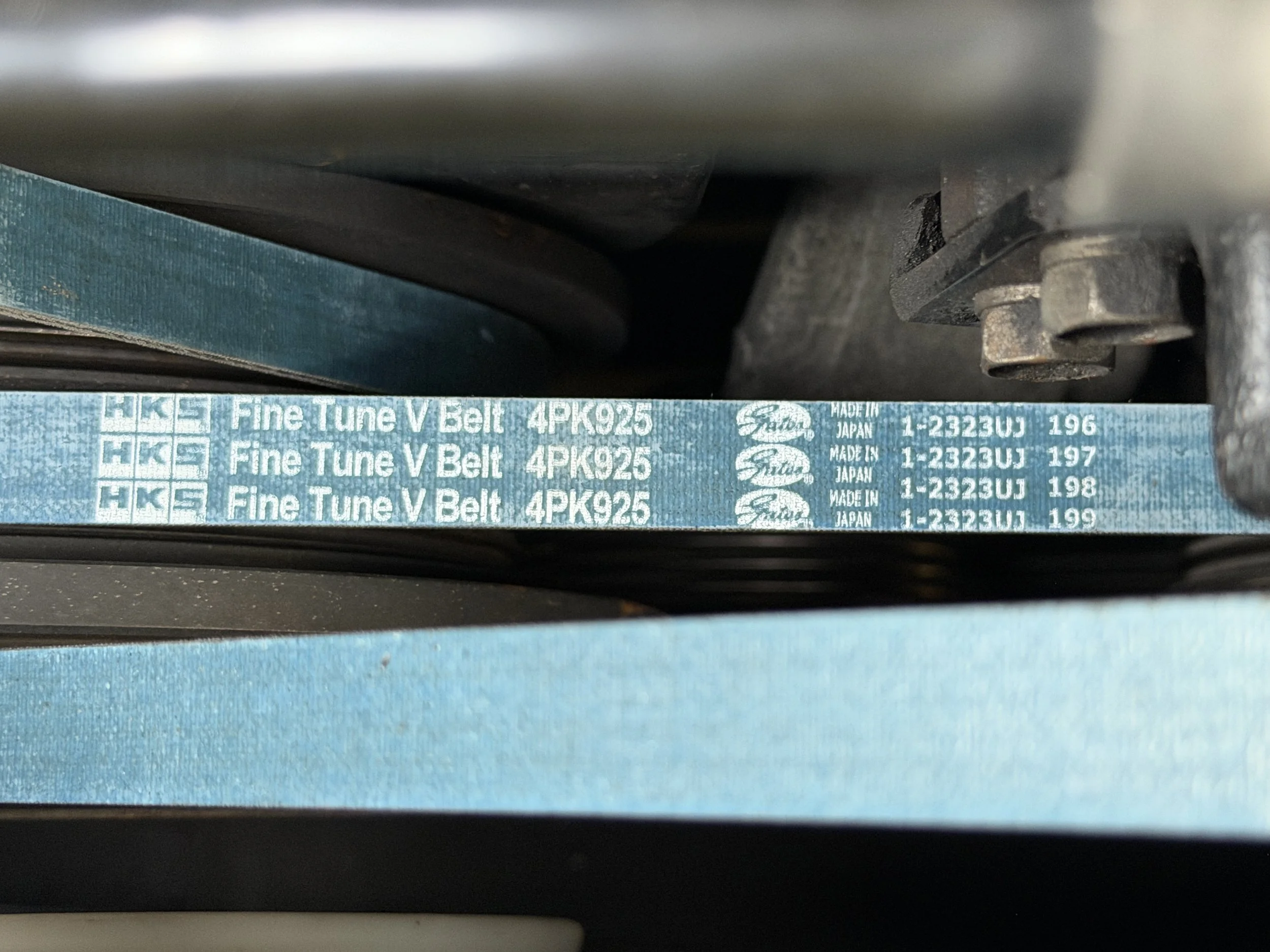 Close-up of a blue mechanical belt labeled 'Fine Tune V Belt 4PK925' with manufacturing information, partially visible, located within machinery or equipment.