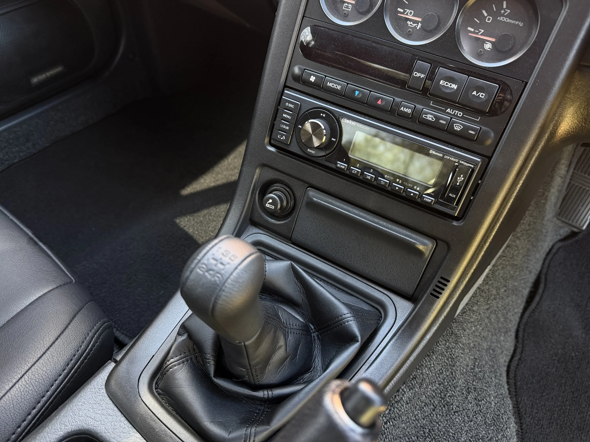 Interior of a car showing a manual gear shifter, dashboard with gauges, and a stereo system.