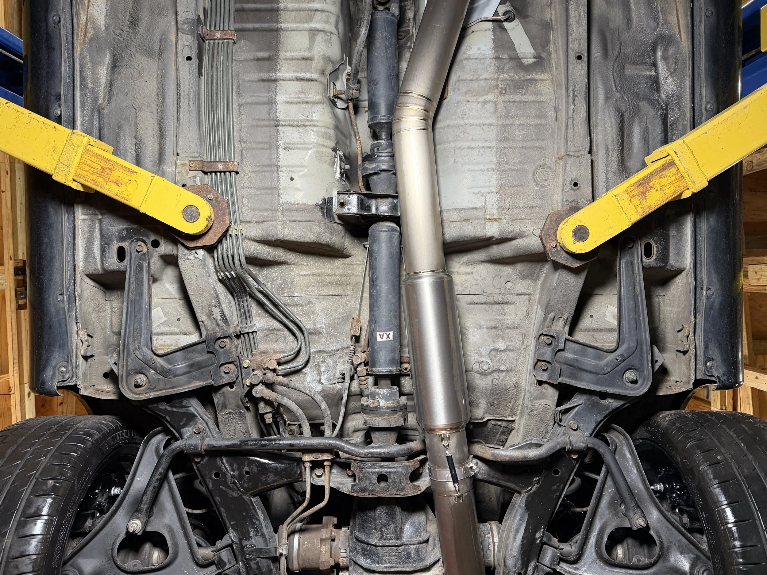 Underneath view of a car lifted on two yellow support stands, showing the undercarriage, exhaust system, suspension, and wheels.