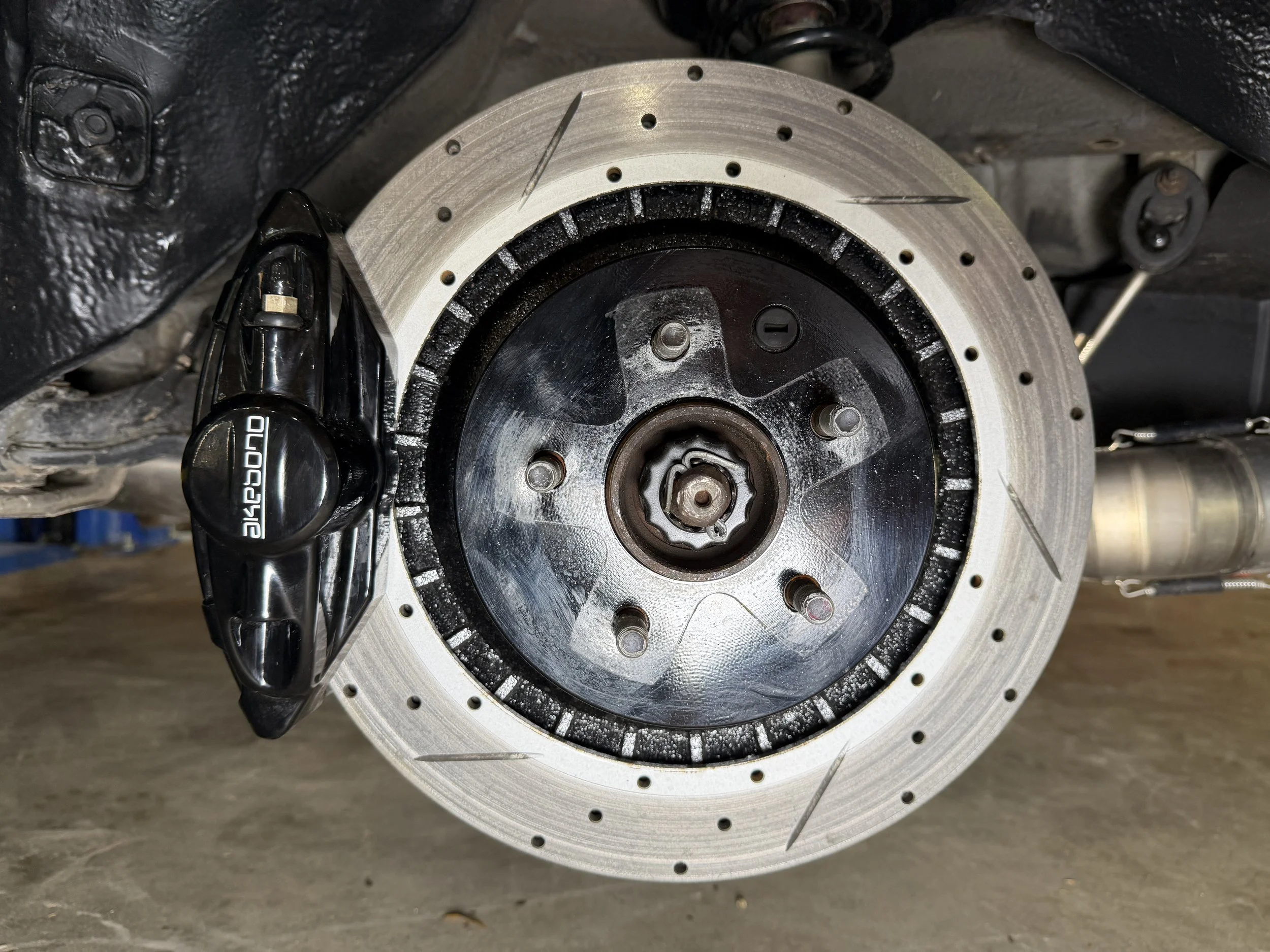 Close-up of a car's front wheel hub with brake disc and part of the suspension, with a black SPARCO-branded component attached.