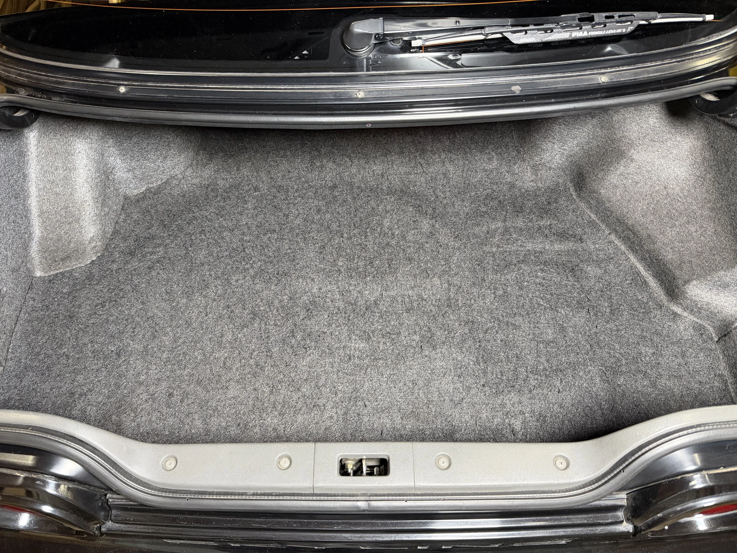 Open car trunk with gray carpeted interior and a folded black suitcase inside.