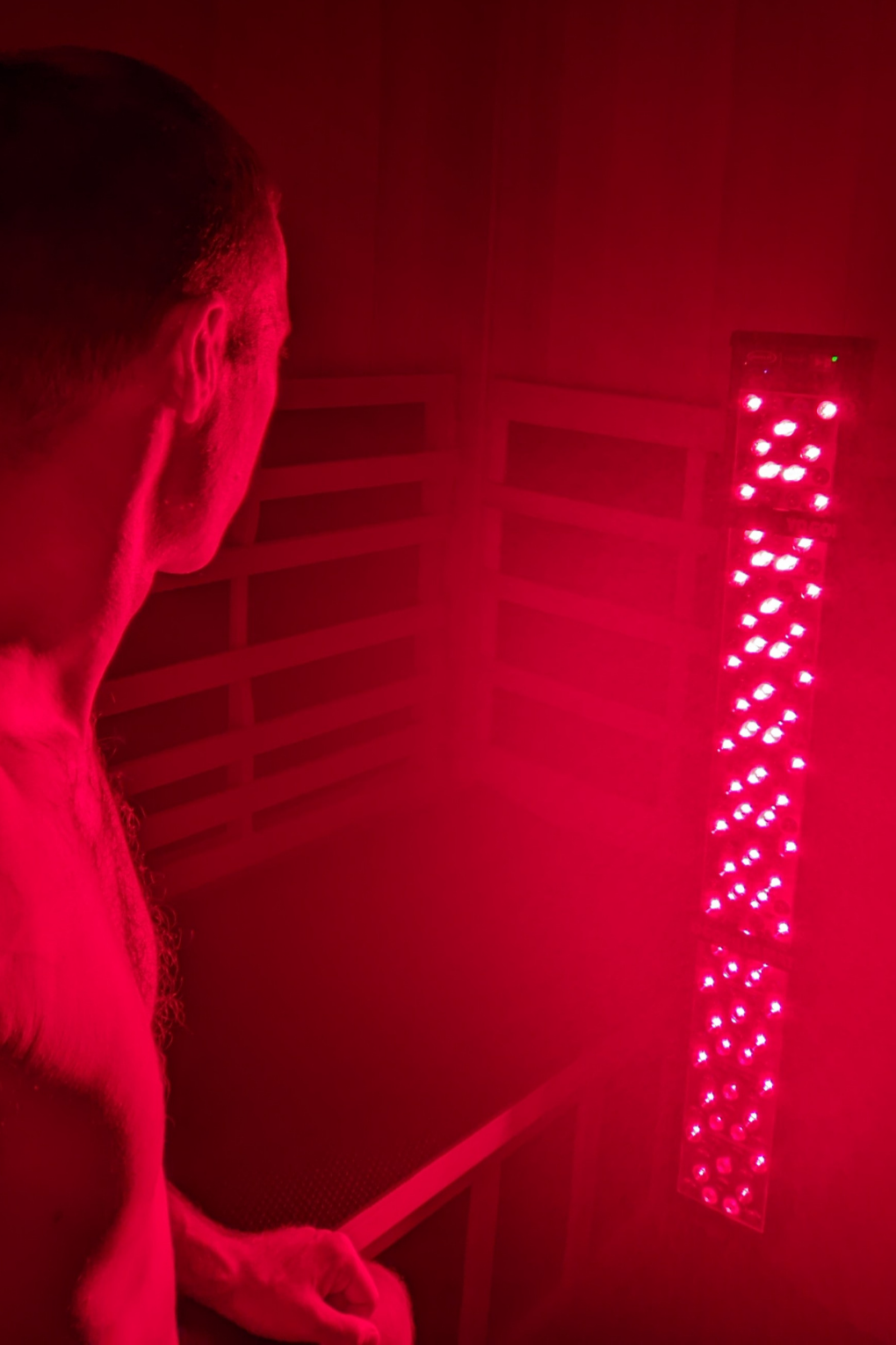 A man stands in a dark room illuminated by red light from a tall LED light panel.