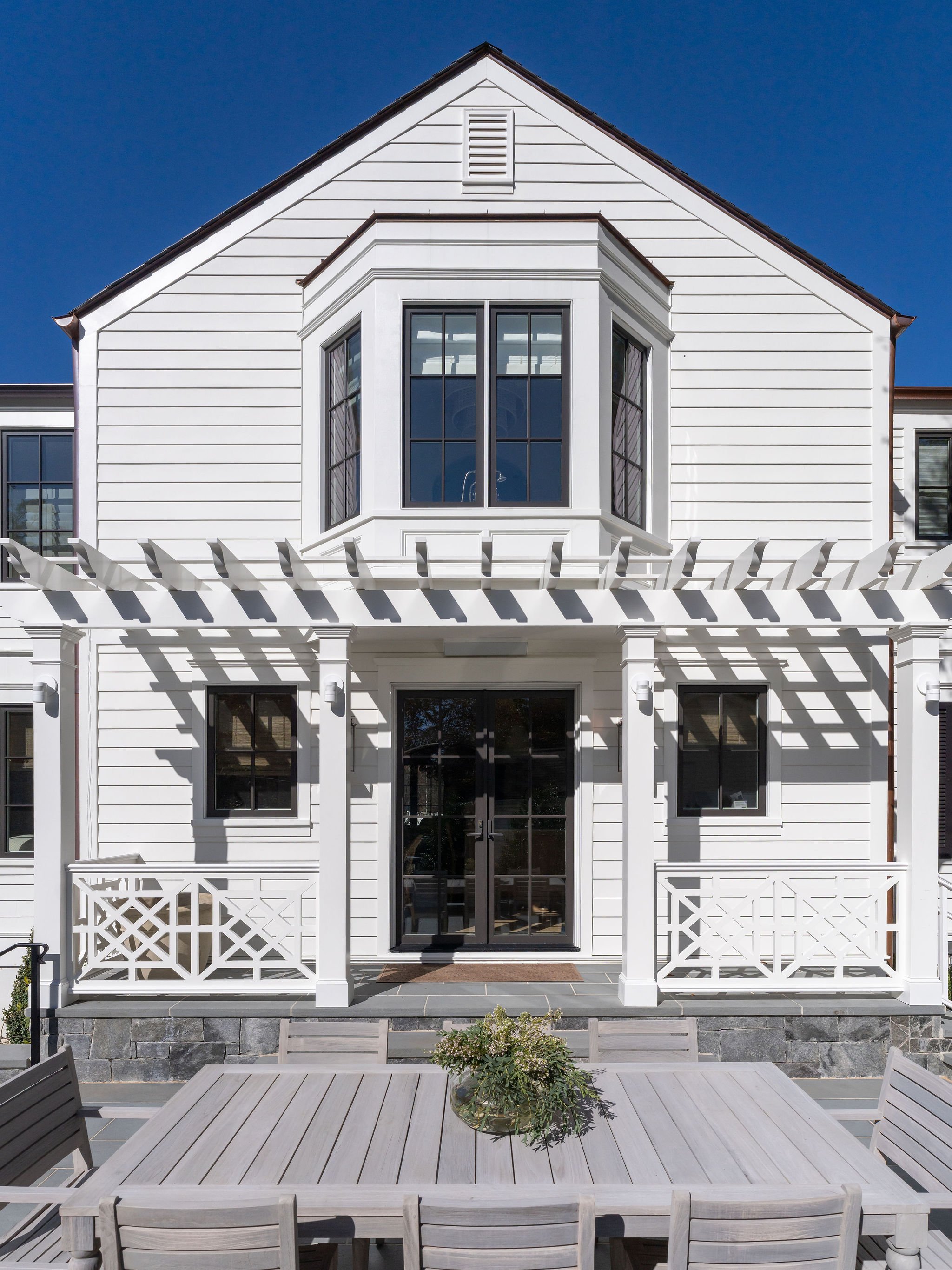 Exterior view of an architectural pergola with teak dining furniture in the foreground. 