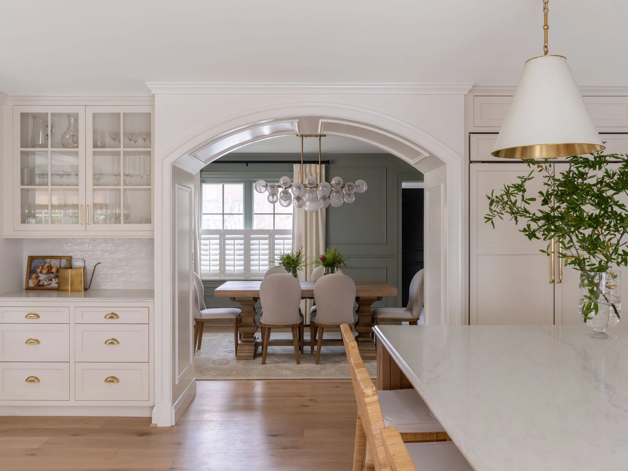 A green jewel-boxed dining room with a sculptural chandelier, framed by an architectural arch.