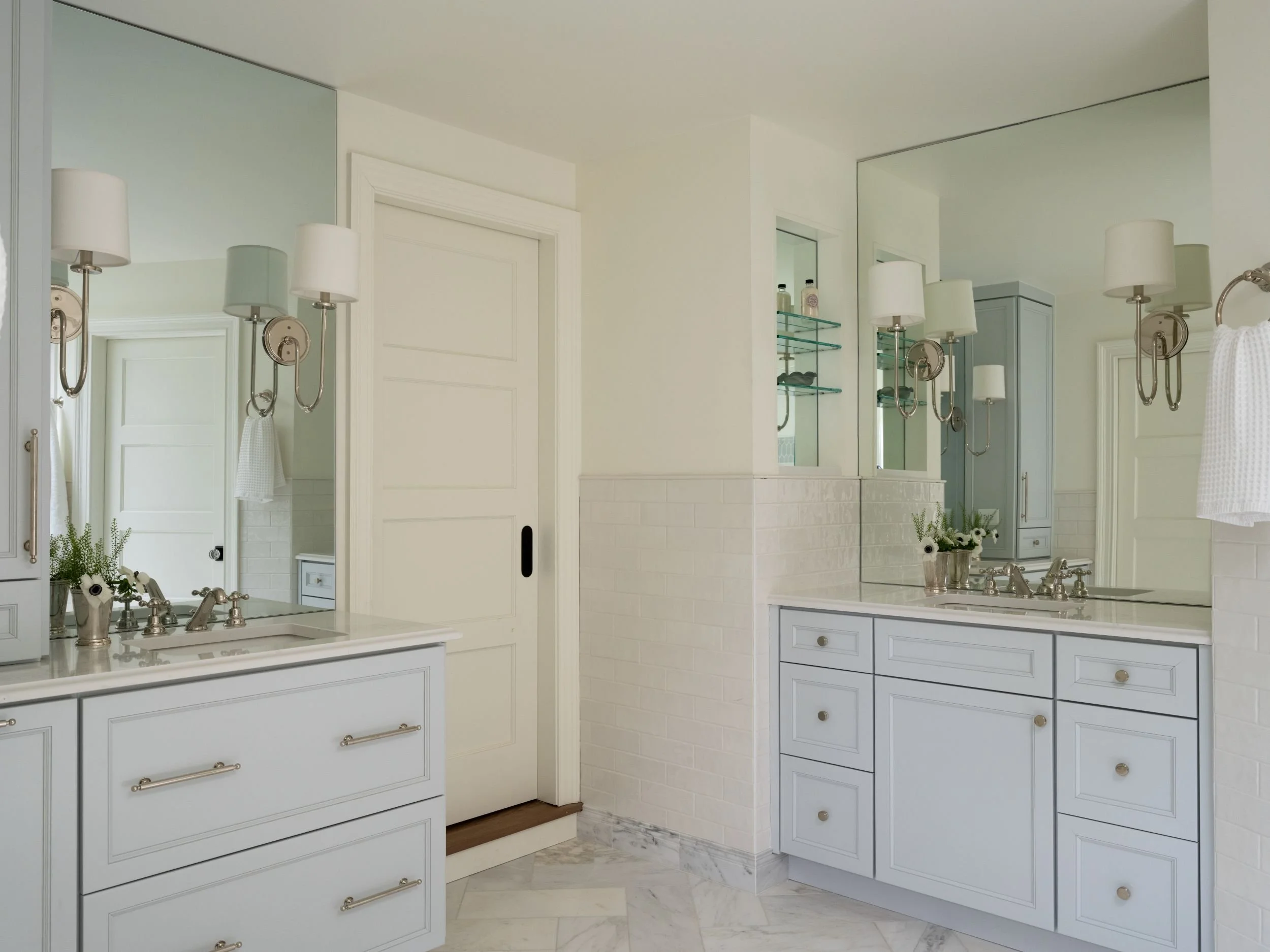 Soft blue bathroom vanities with large mirror glass and shaded sconces. 