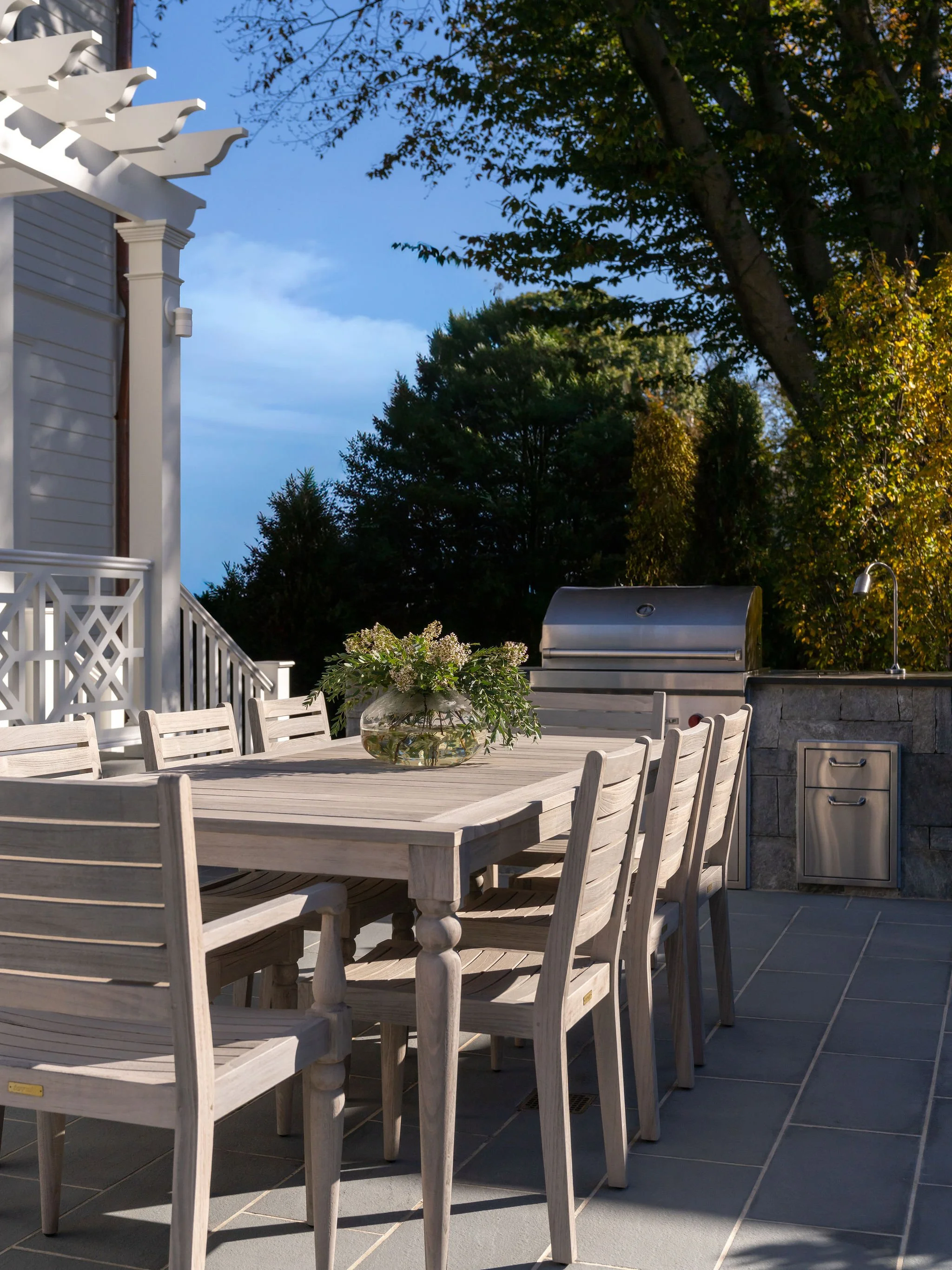 A teak outdoor dining set on a flagstone patio. 