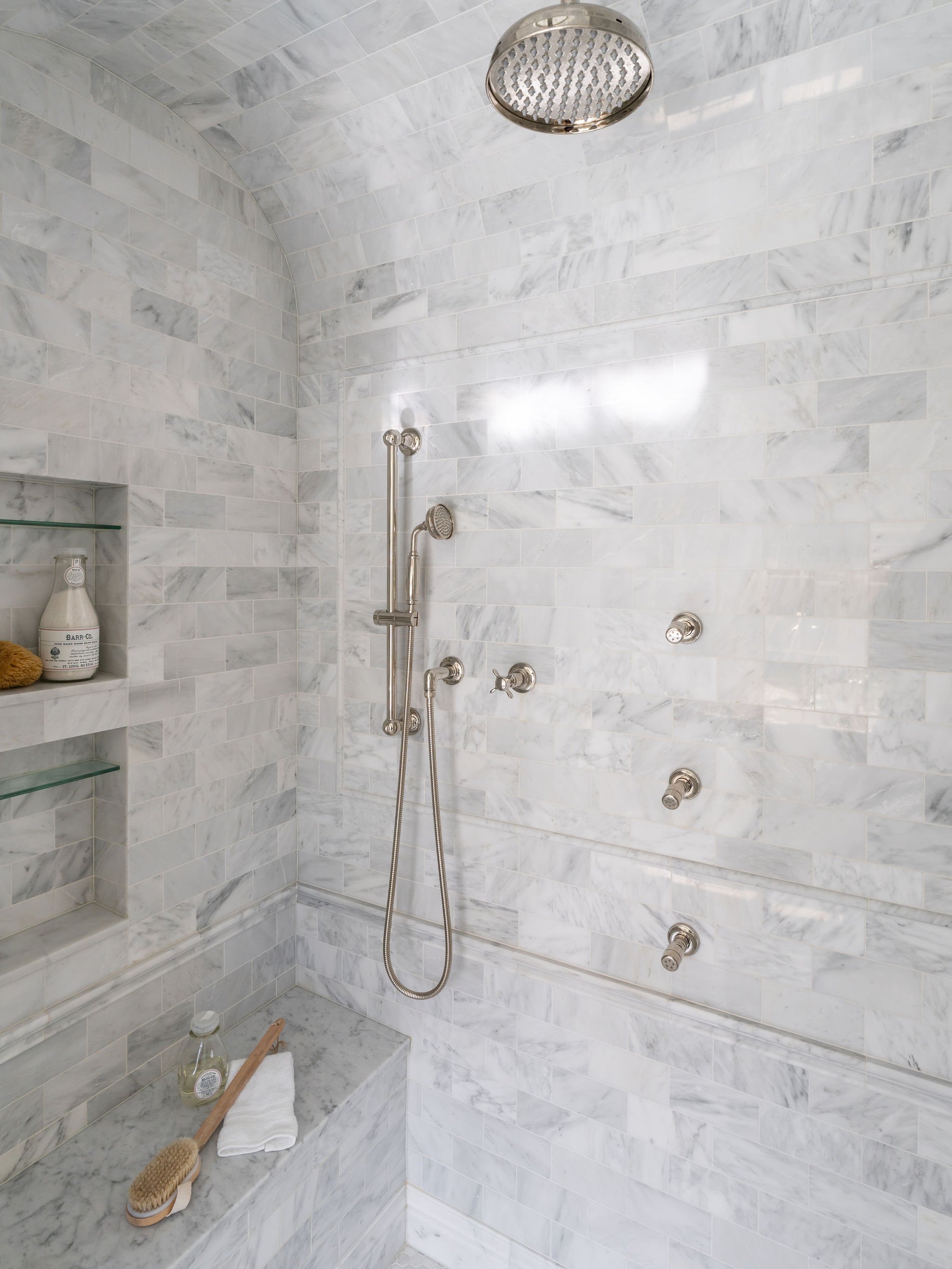 A marble shower with bench and niches, curved ceiling detail, and polished nickel plumbing fixtures.