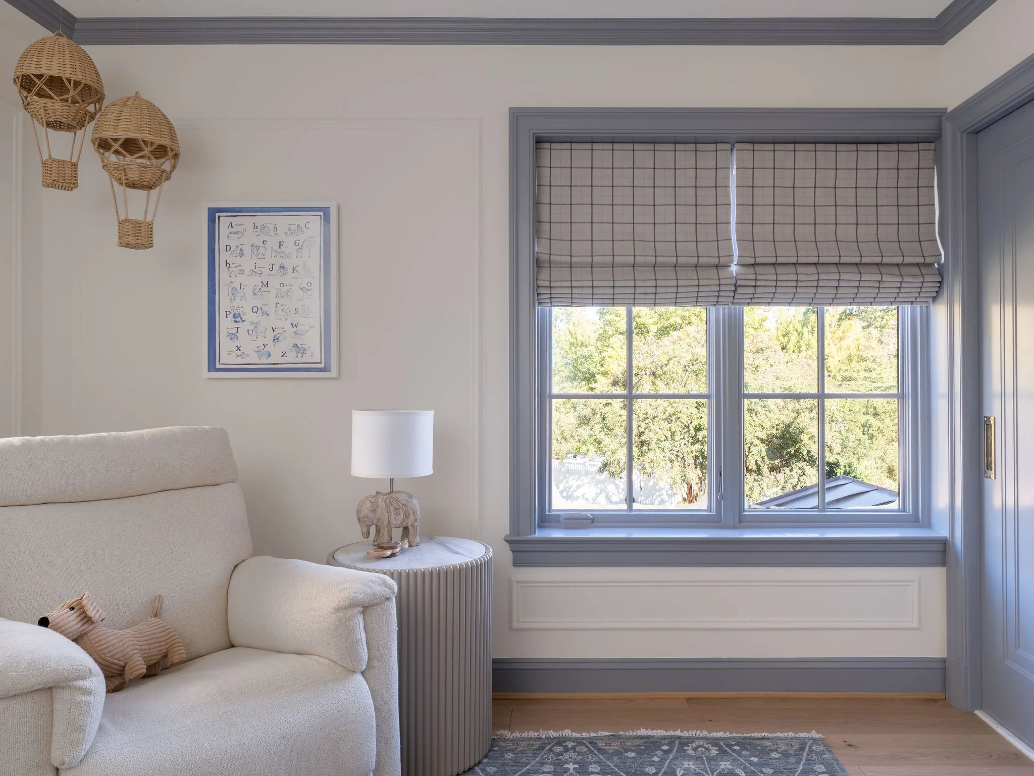 A nursery with blue contrast trim, custom plaid roman shades and a cozy upholstered rocking chair. 