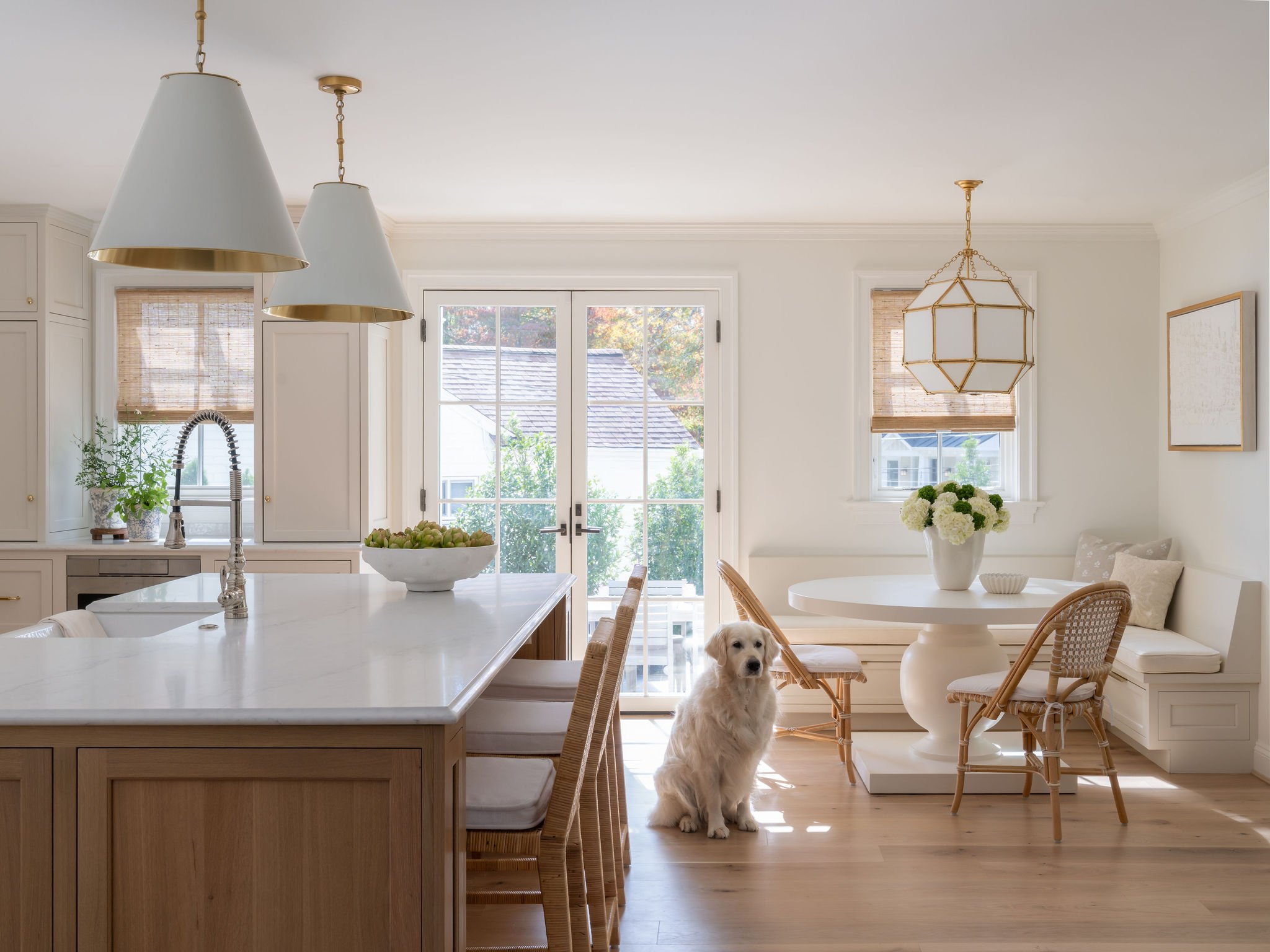 A kitchen bright with natural light adjacent to a cozy breakfast nook banquette. A golden retriever is patiently sitting in the background. 