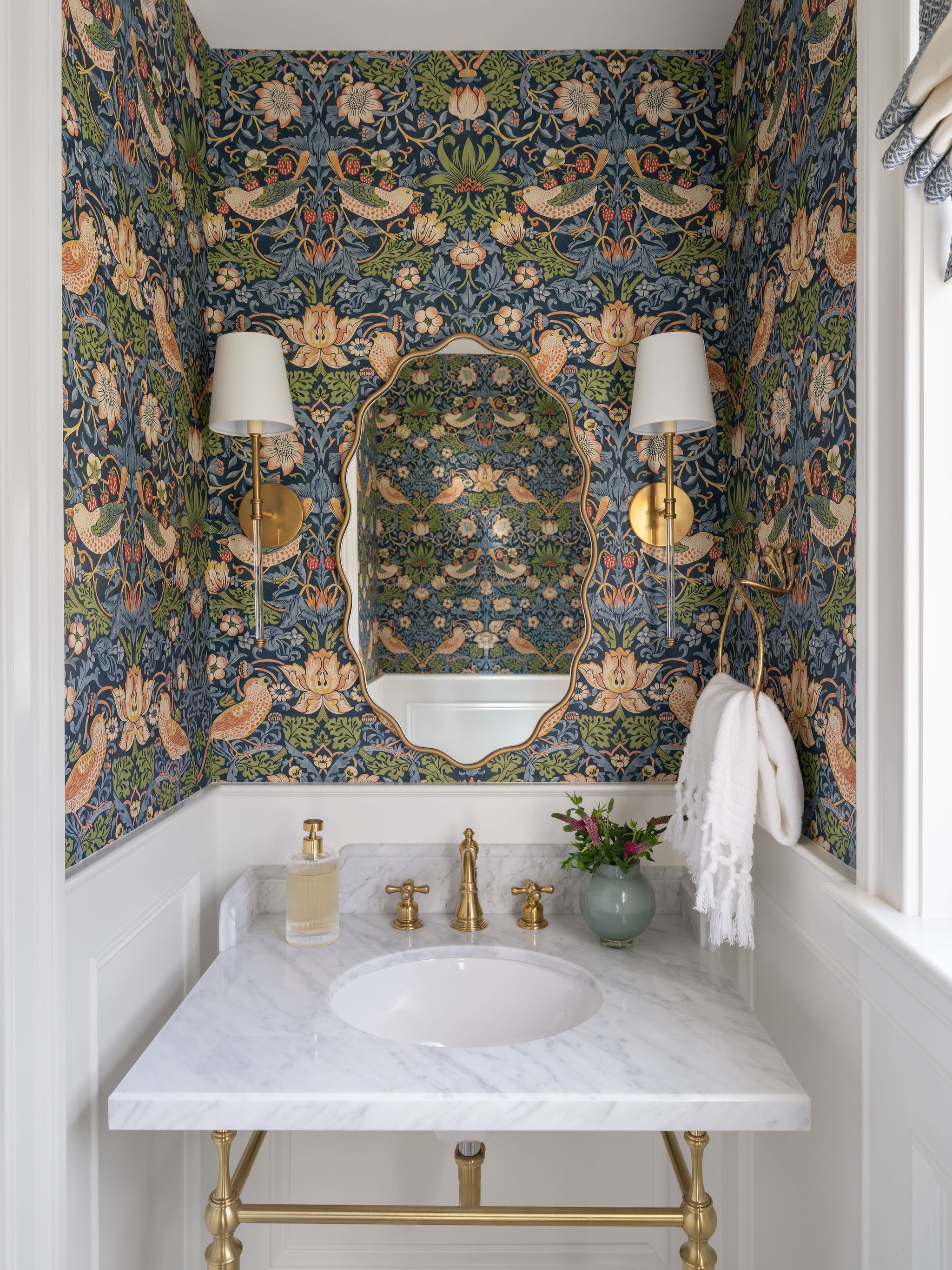 A playful powder room with whimsical wallpaper, bright wainscotting and brass fixtures. 
