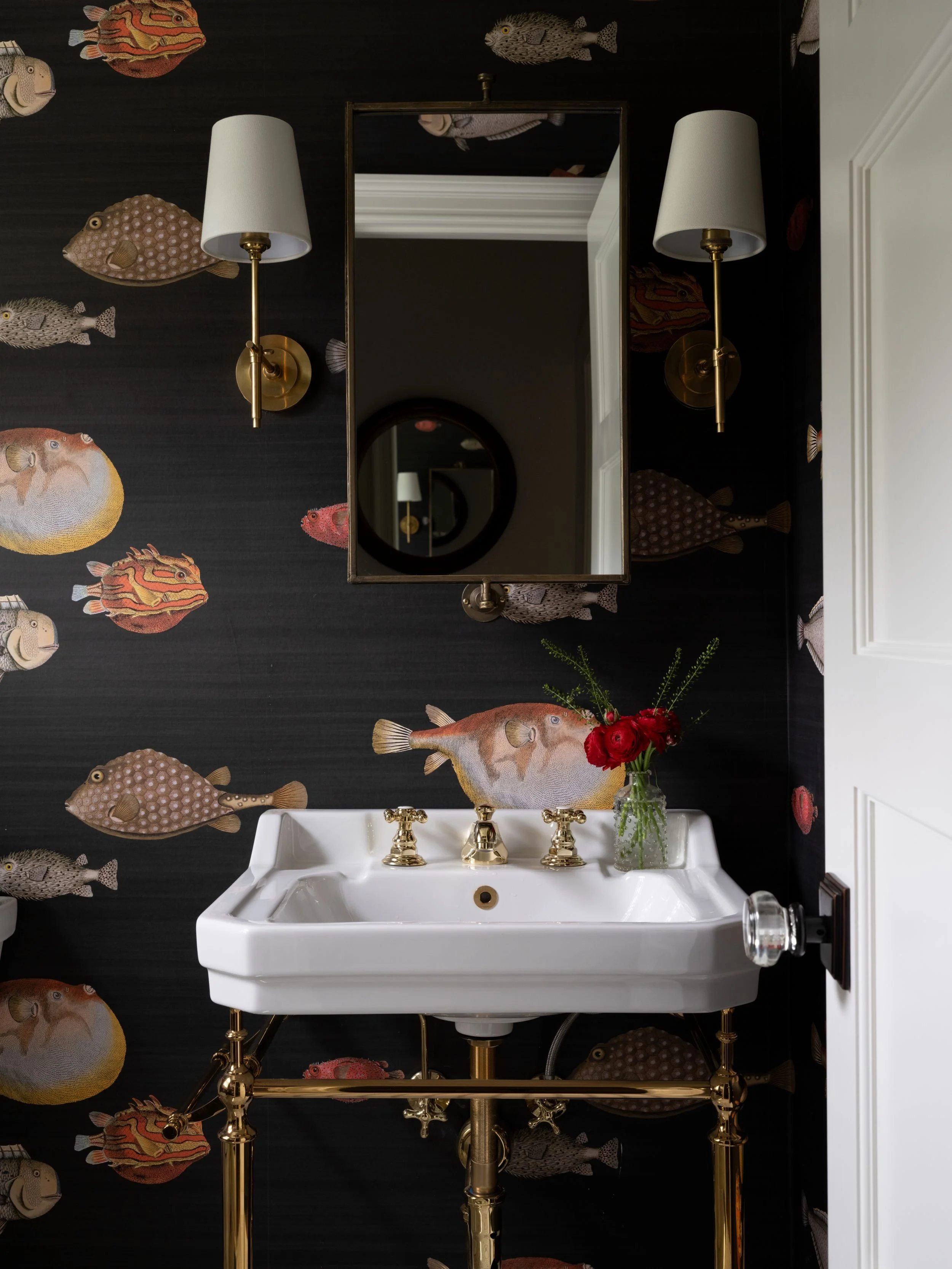 Dramatic fish wallpaper with black background and pedestal sink, with shaded wall sconces and mirror. 