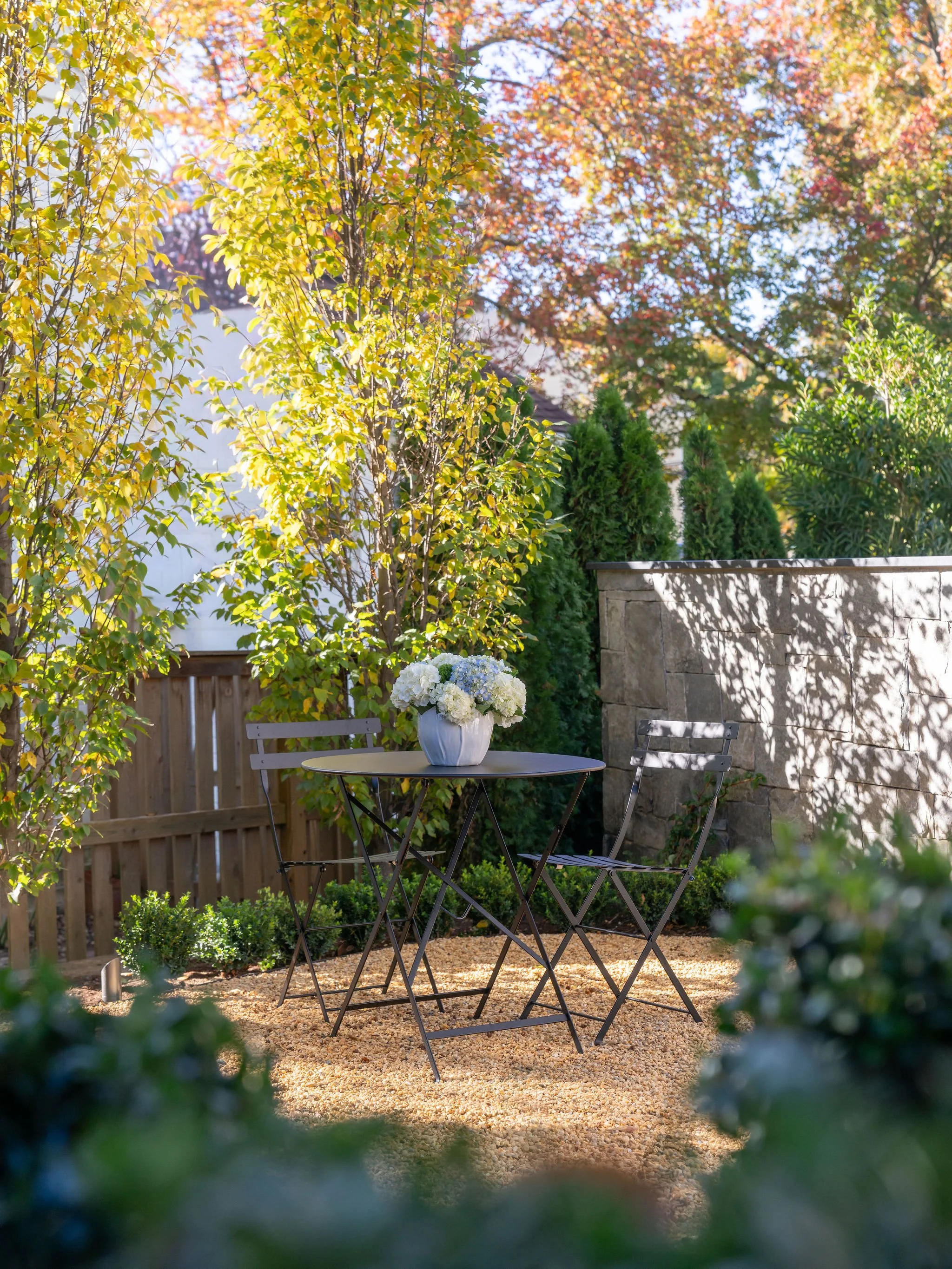 A backyard oasis with a bistro table and a hydrangea floral arrangement. 