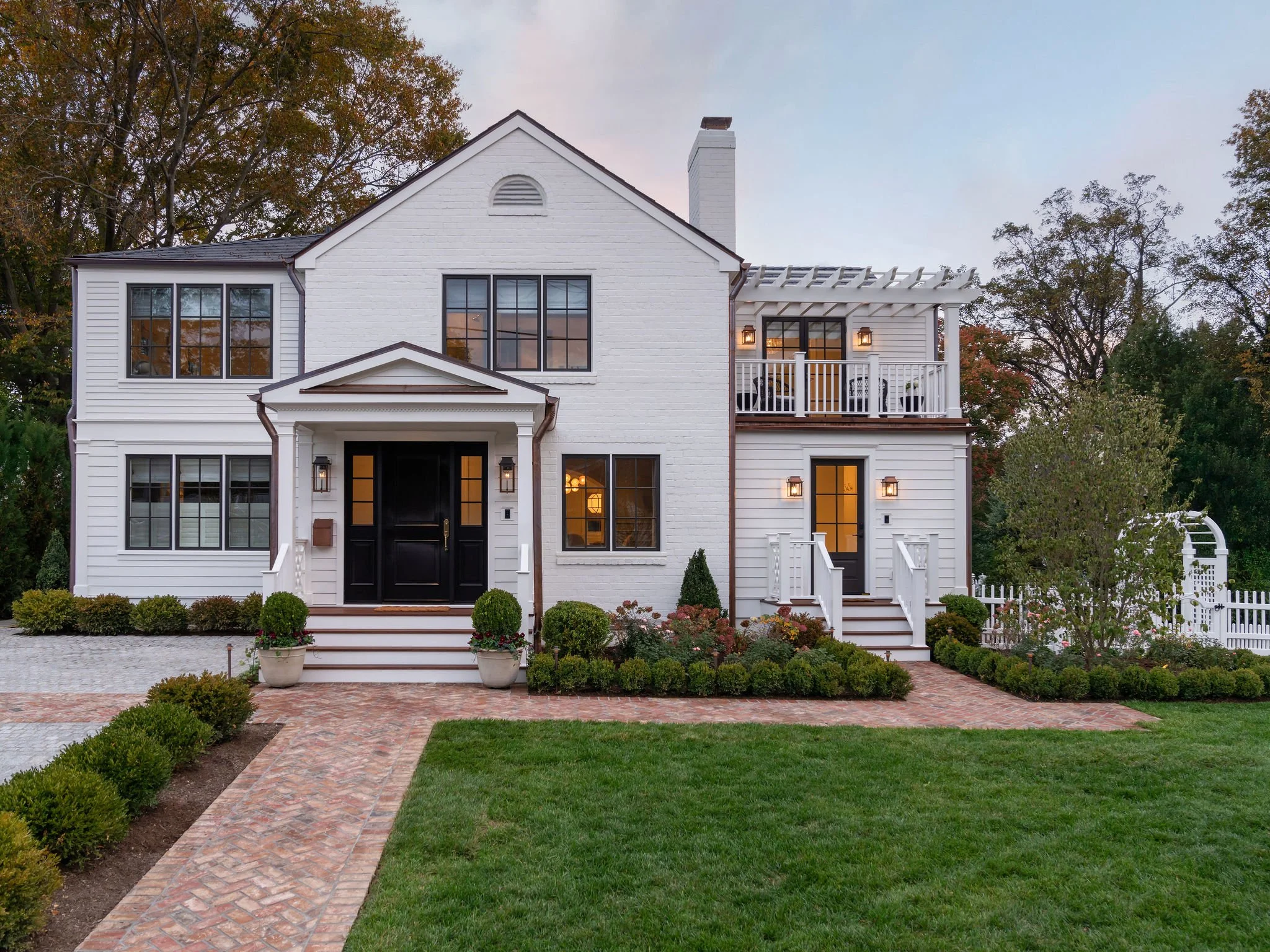 Exterior view of a white brick and siding house with a red brick sidewalk and black window and door details. 