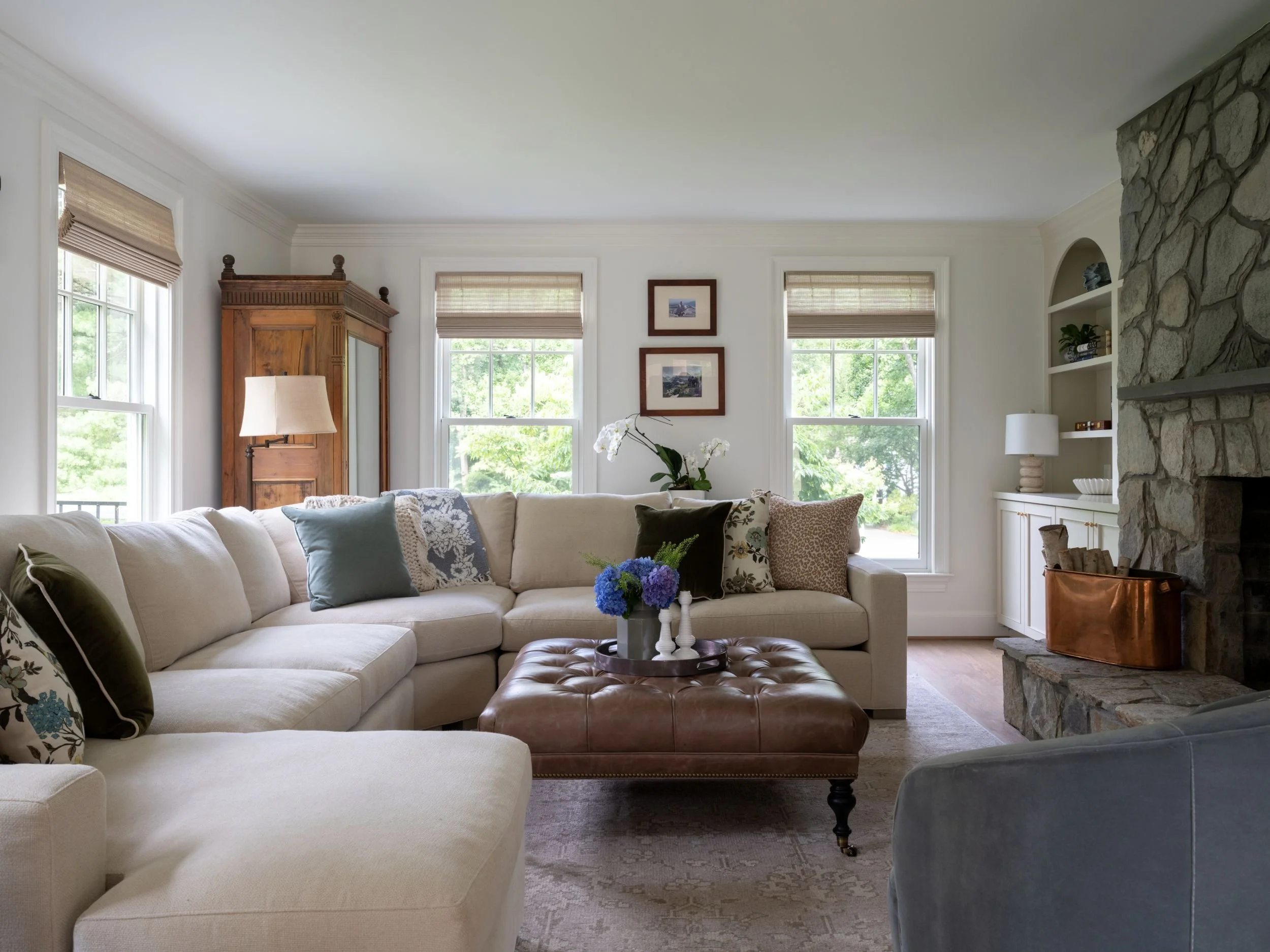 Cozy living room with stone fireplace and cream sectional, with a tufted leather ottoman.