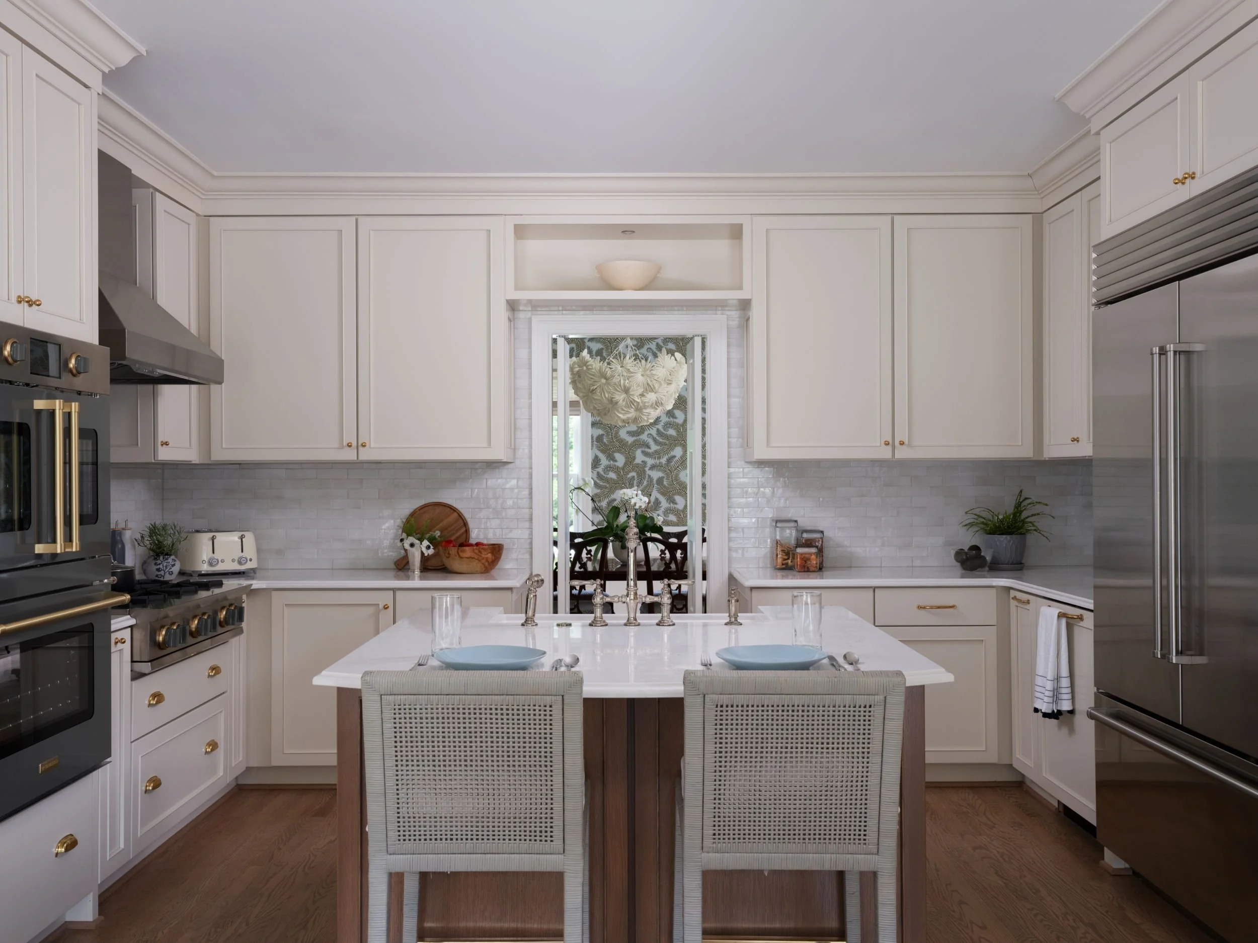 Cream kitchen with custom color green appliances and view into the dining room, with palm wallpaper and decorative chandelier.