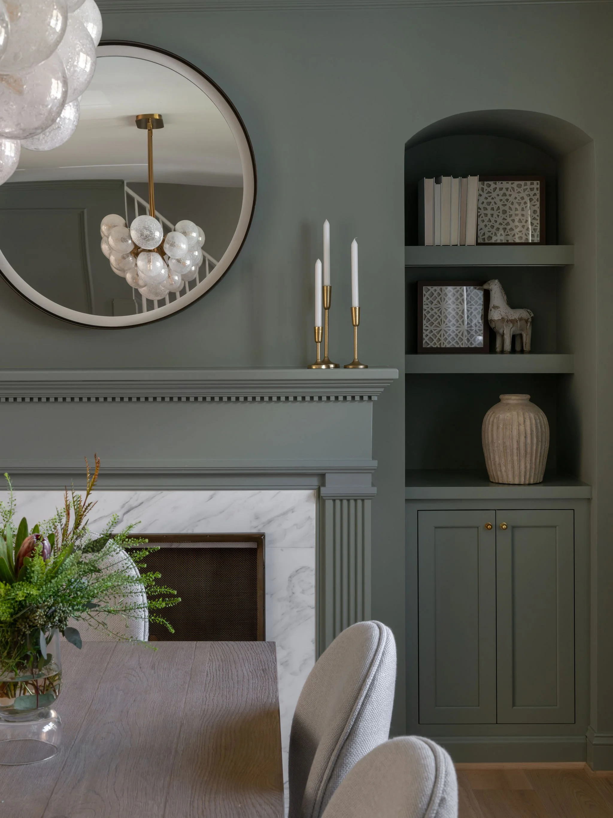 A moody green dining room featuring a marble fireplace surround and built-in cabinetry. 