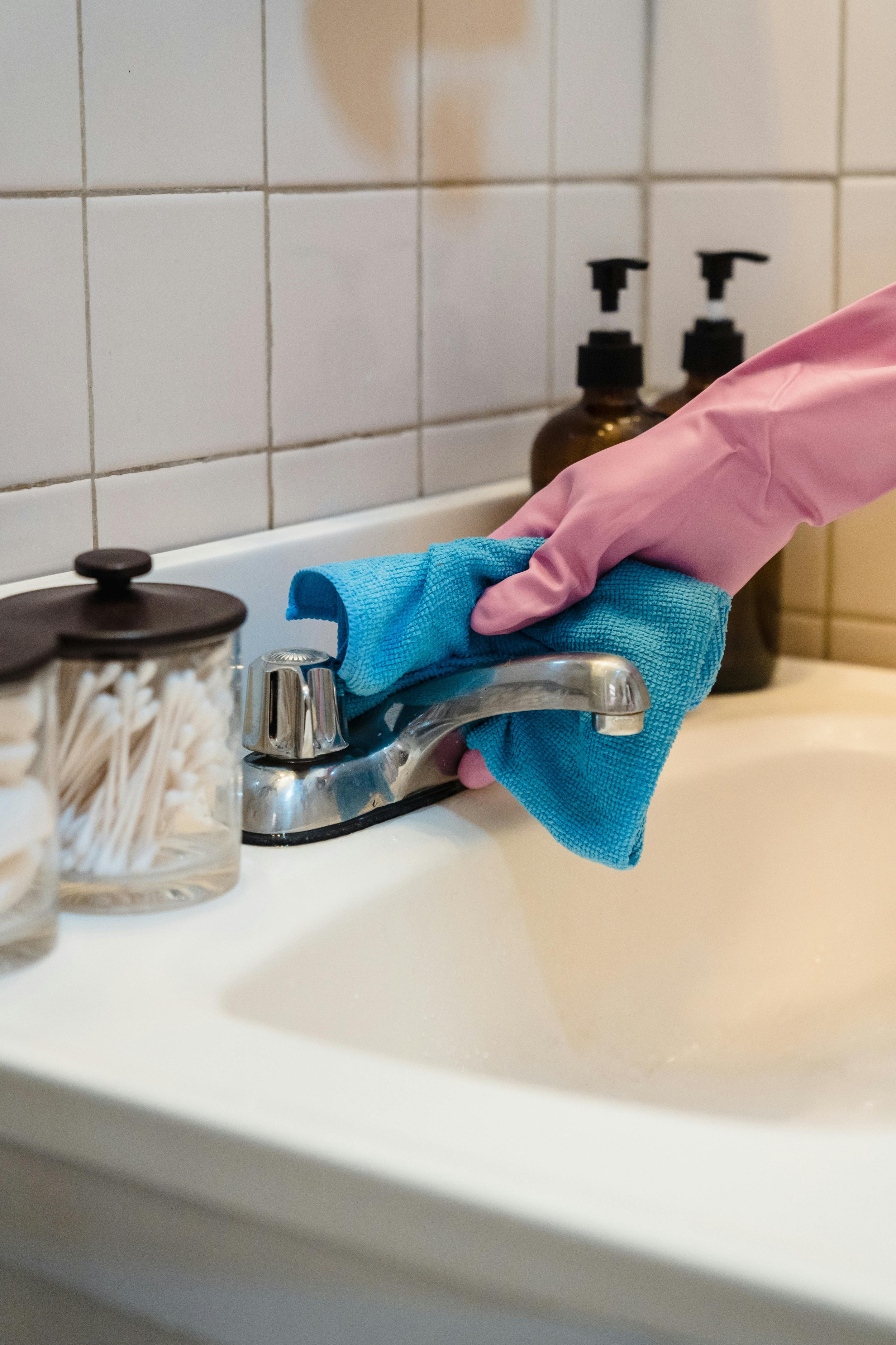 A person wearing pink gloves cleaning a bathroom sink with a blue cloth.