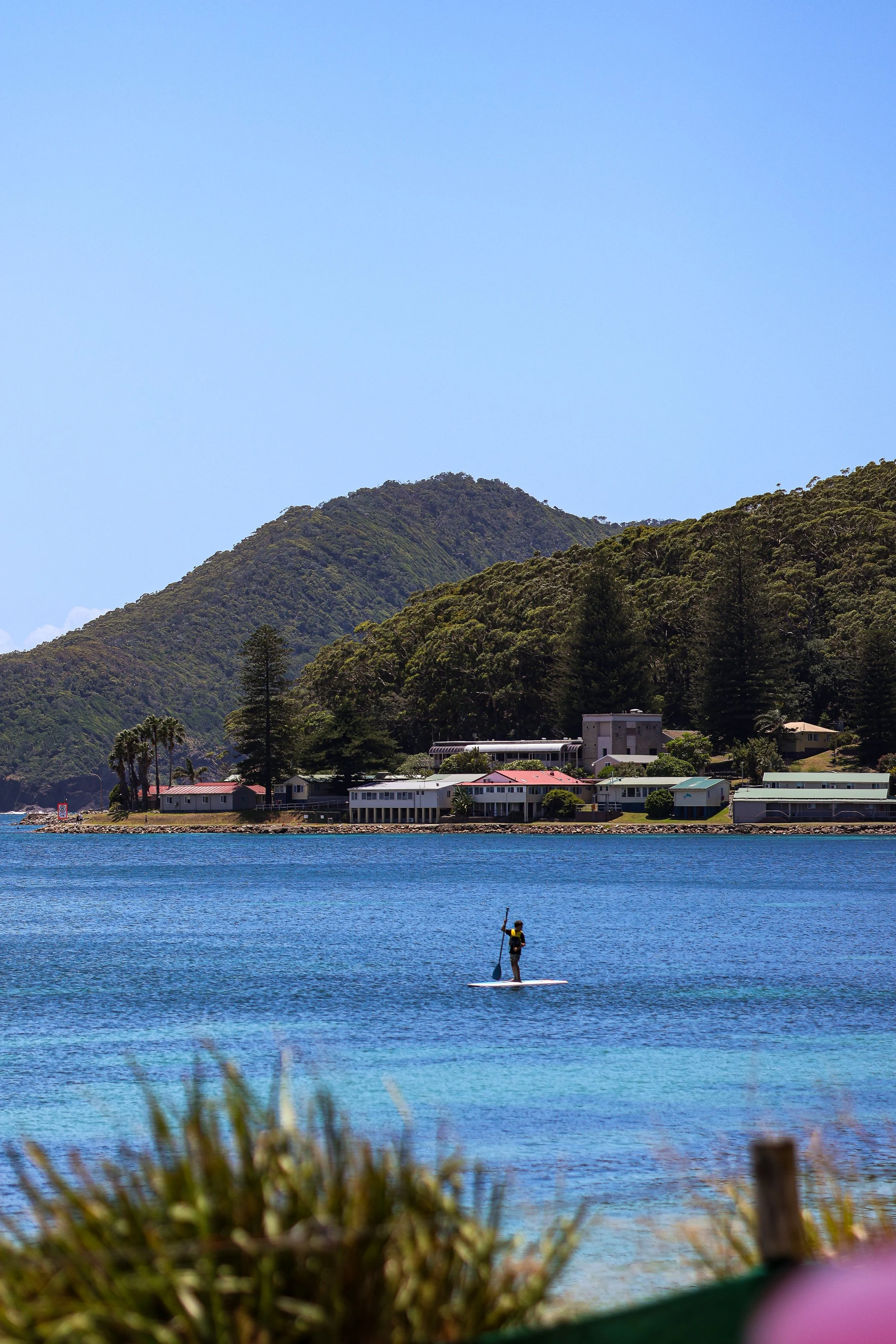 A person paddleboarding on a calm body of water in front of a mountainous landscape with houses.