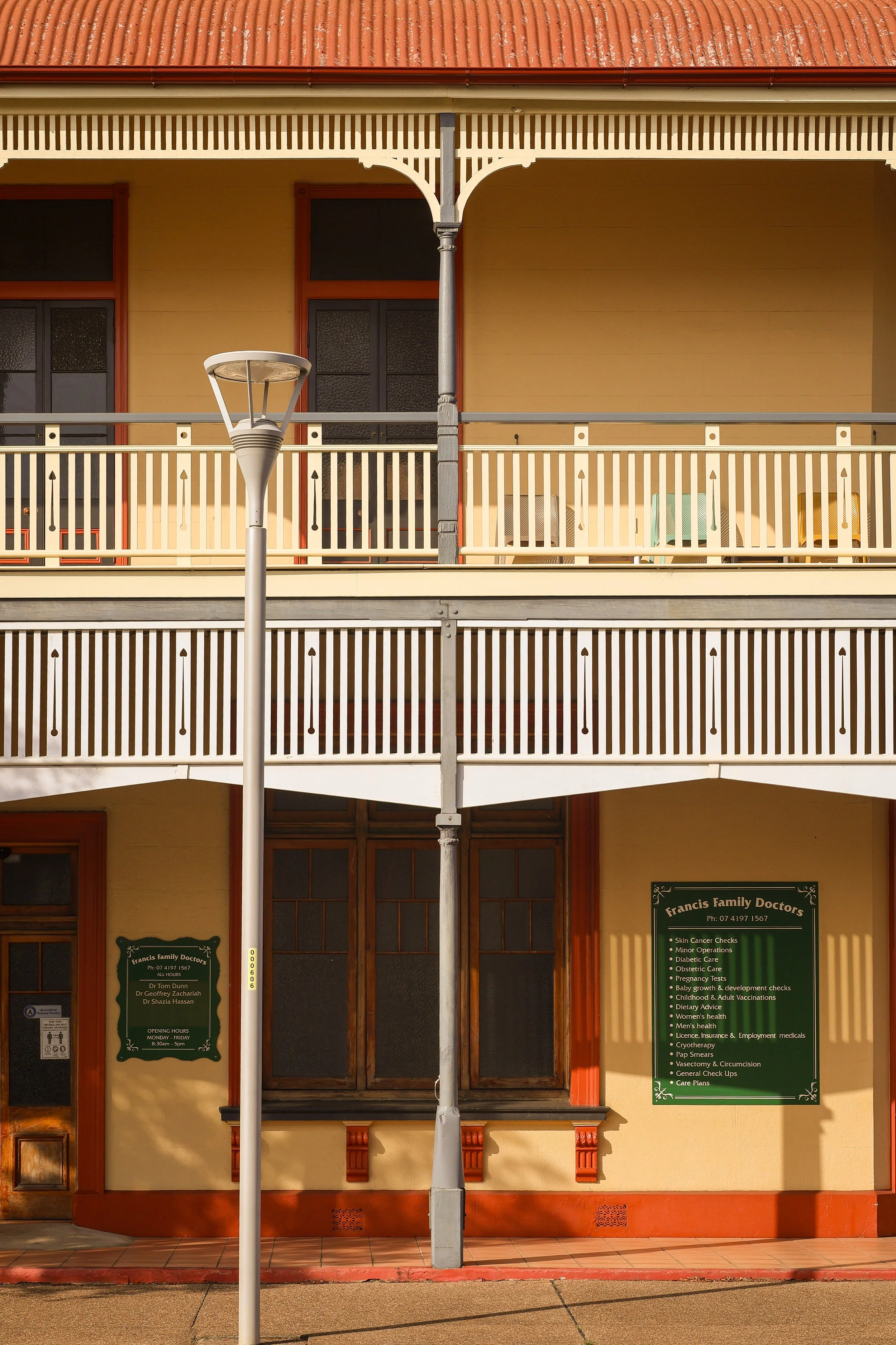 The image shows the exterior of a building with a beige facade, red trim around the windows, and a red-tiled roof. There are two large windows and a green sign advertising a medical practice named Francis Family Doctors, listing services offered.