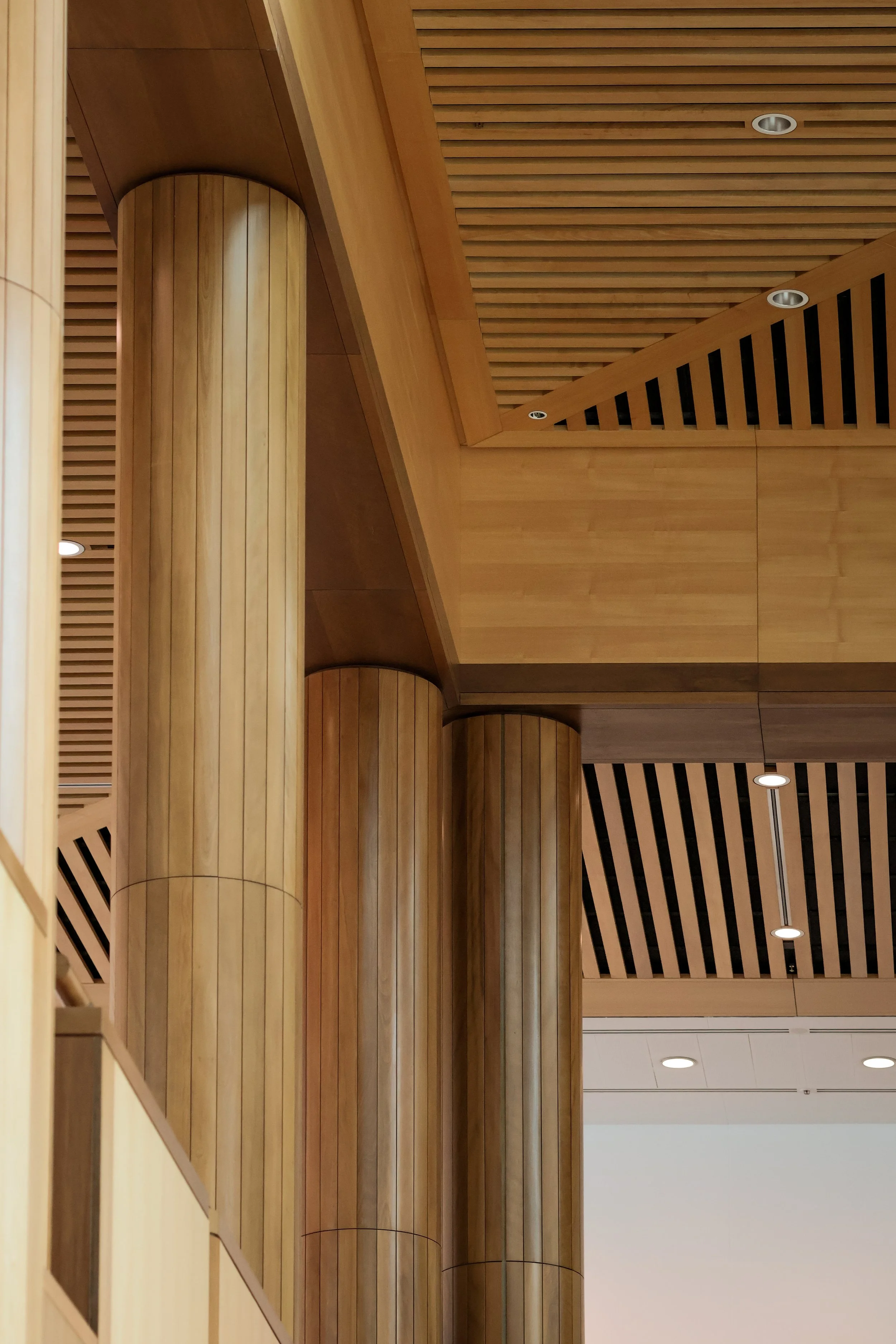 Wooden pillars and ceiling with recessed lighting and slatted wood paneling in a modern interior space.