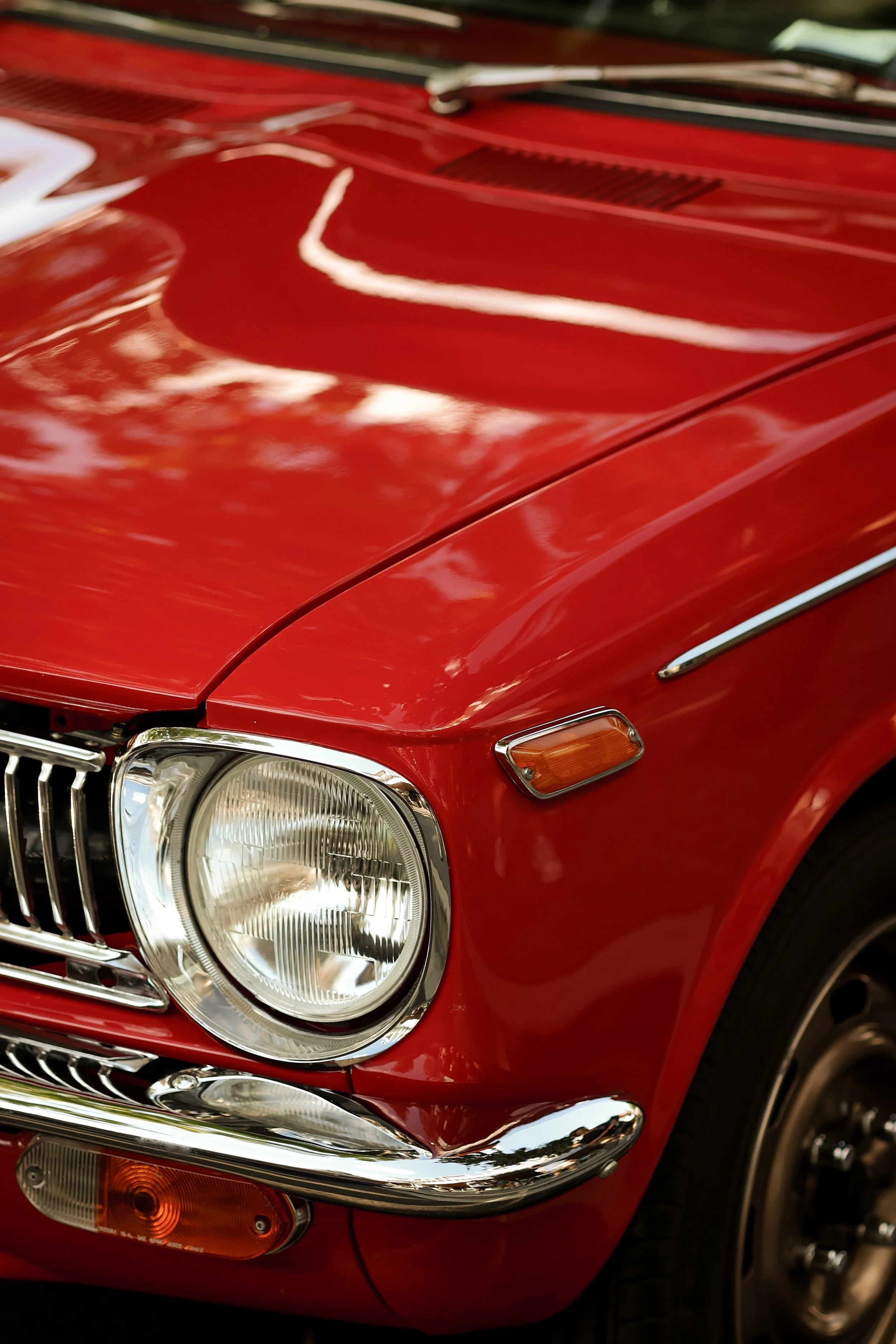 Close-up of the front part of a red classic car, showing the headlight, grille, and turn signal.