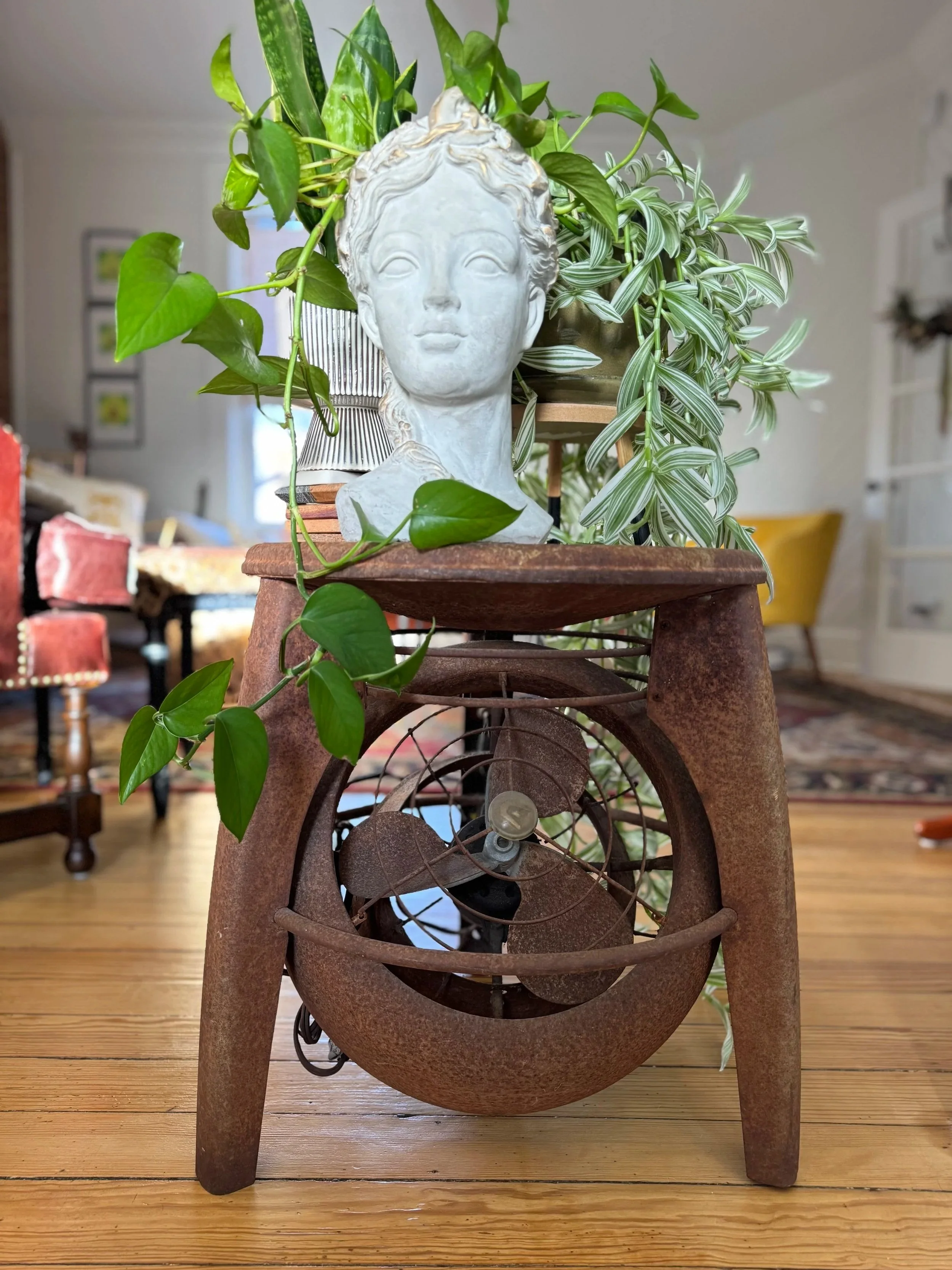White bust planter with trailing plants on a rusty vintage stand with an old fan inside