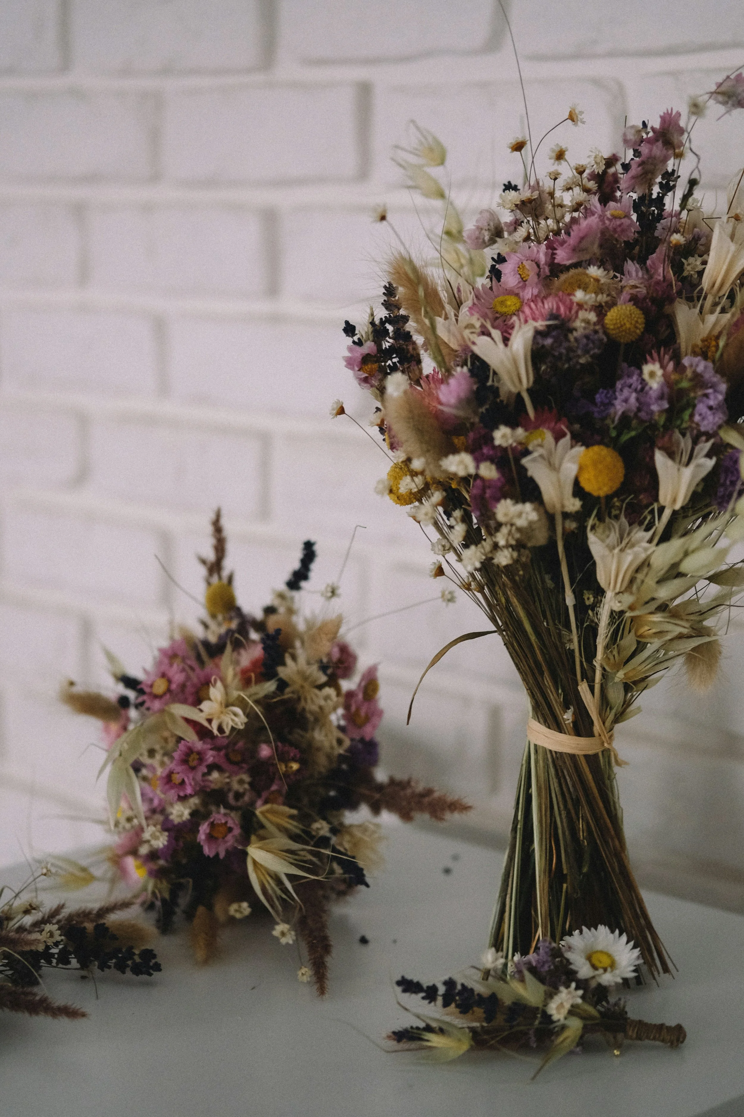 Bouquets of dried flowers on a white surface with a white brick wall background. Manitoba Marriage Commissioner.