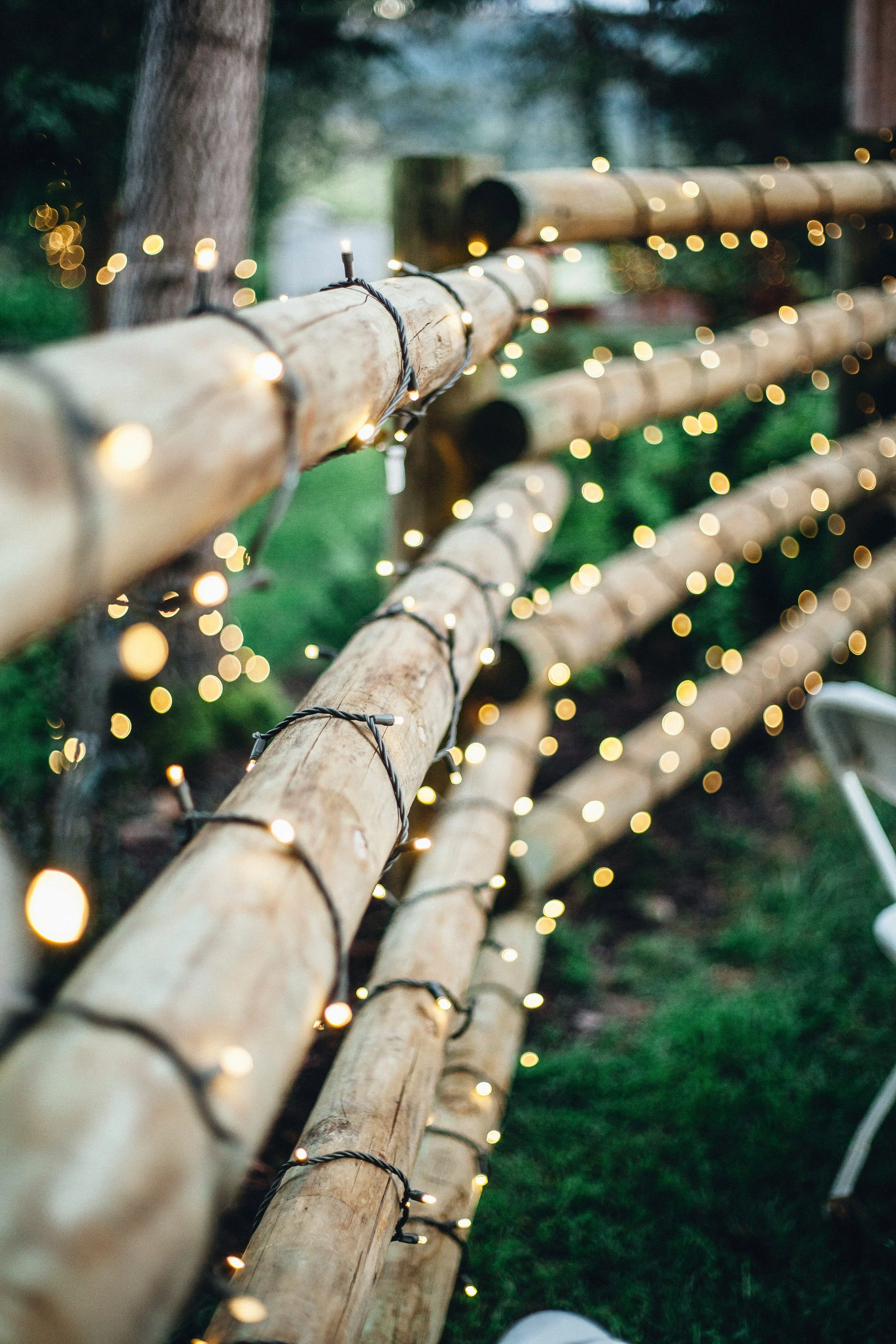 Wooden fence with string lights wrapped around, outdoors, blurred background. Manitoba Marriage Commissioner.