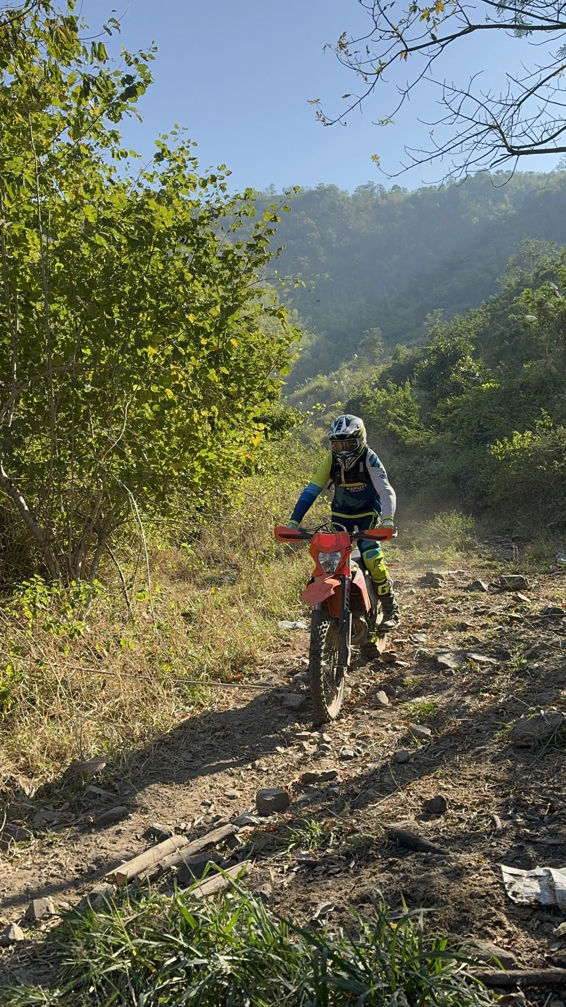 Rider on a red enduro bike climbing a rugged forest trail surrounded by green hills — Thailand off-road adventure and enduro tour