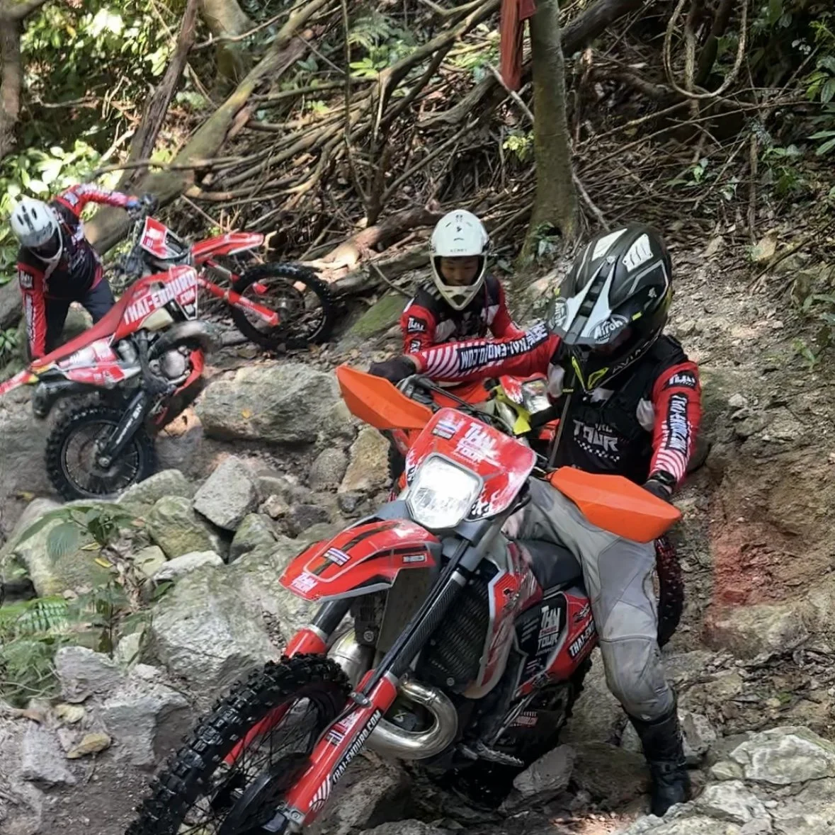Hard enduro riders climbing rocky forest trail in Thailand wearing full protective gear