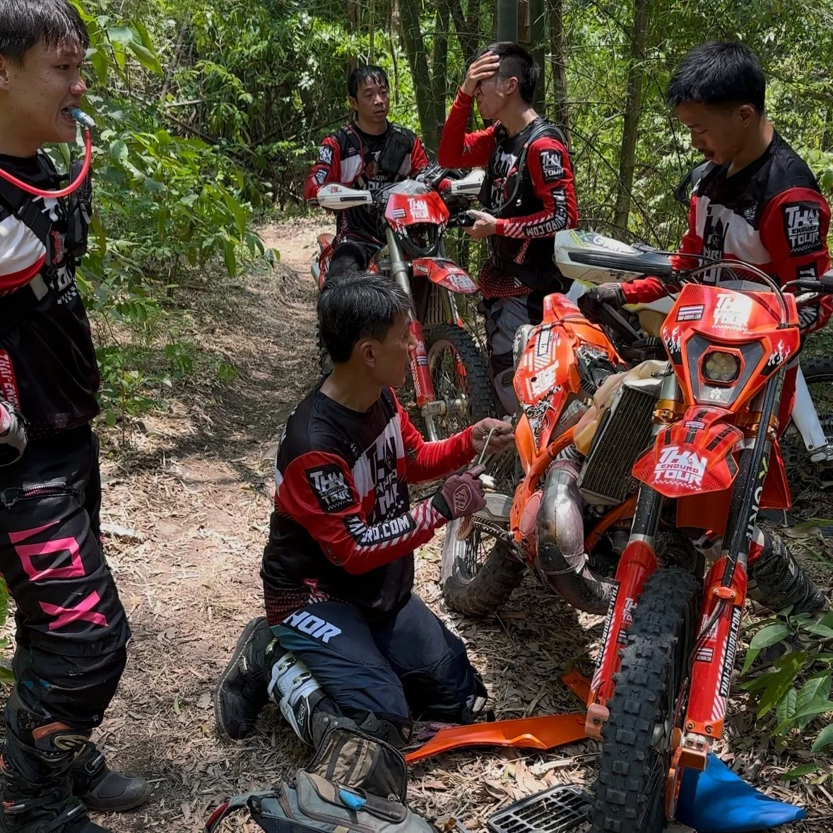 Hard enduro riders repairing KTM dirt bikes on challenging forest trail during Thailand enduro tou