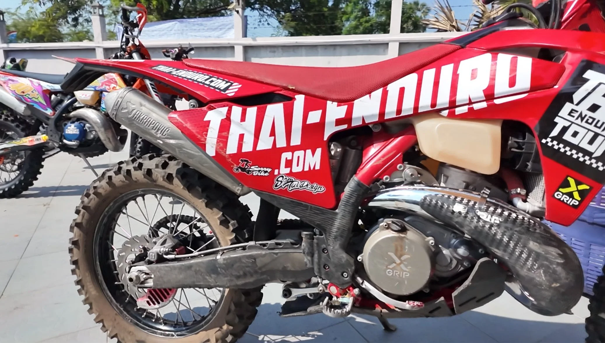 Red off-road motorcycle with mud tires, large exhaust, and multiple sponsor stickers.