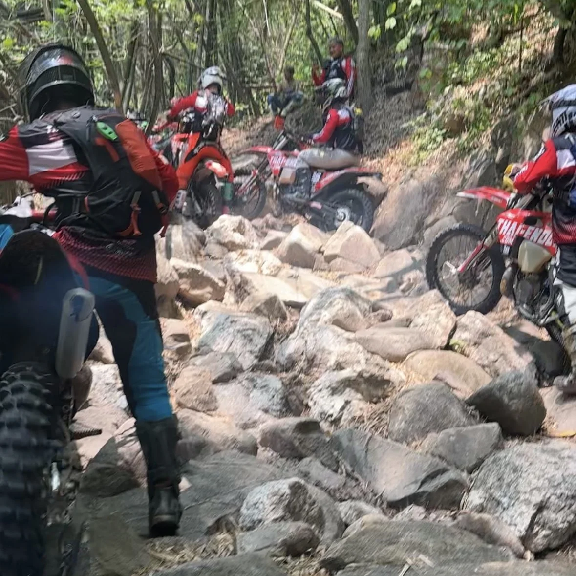 Dirt bike riders tackling technical rocky enduro trail deep in Thai forest
