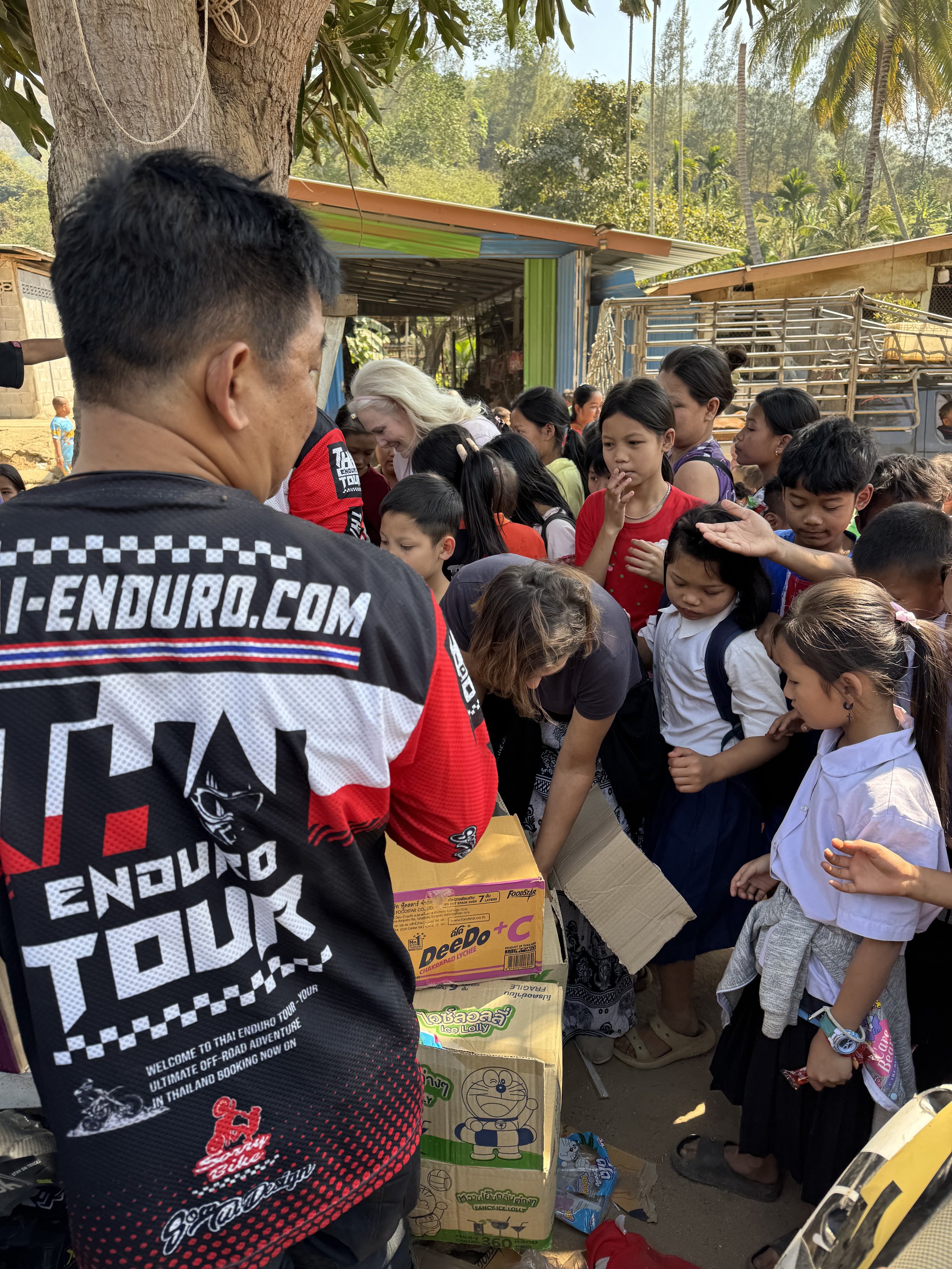 Enduro motorcycle tour riders delivering goods to local children in northern Thailand village during jungle route