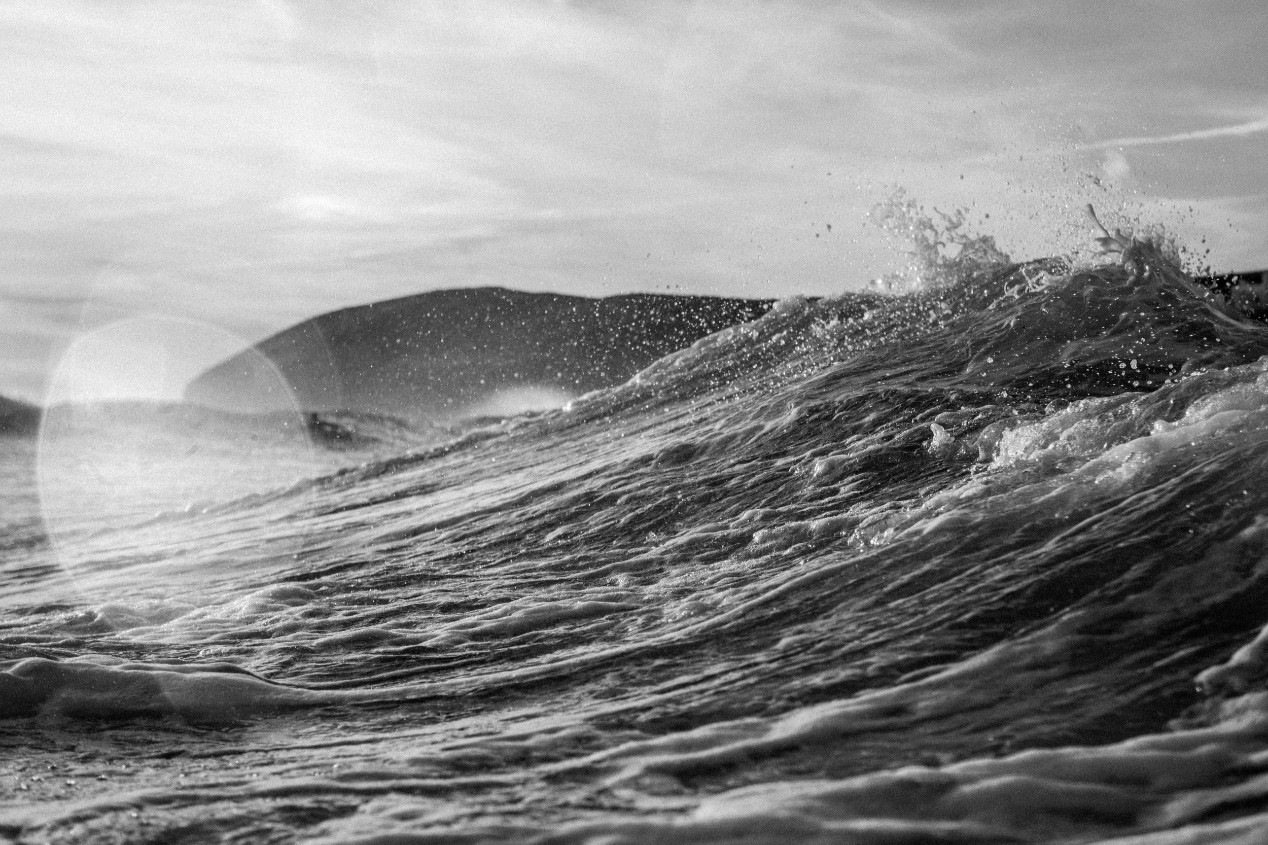 Black and white photograph of ocean waves with hills in the background.