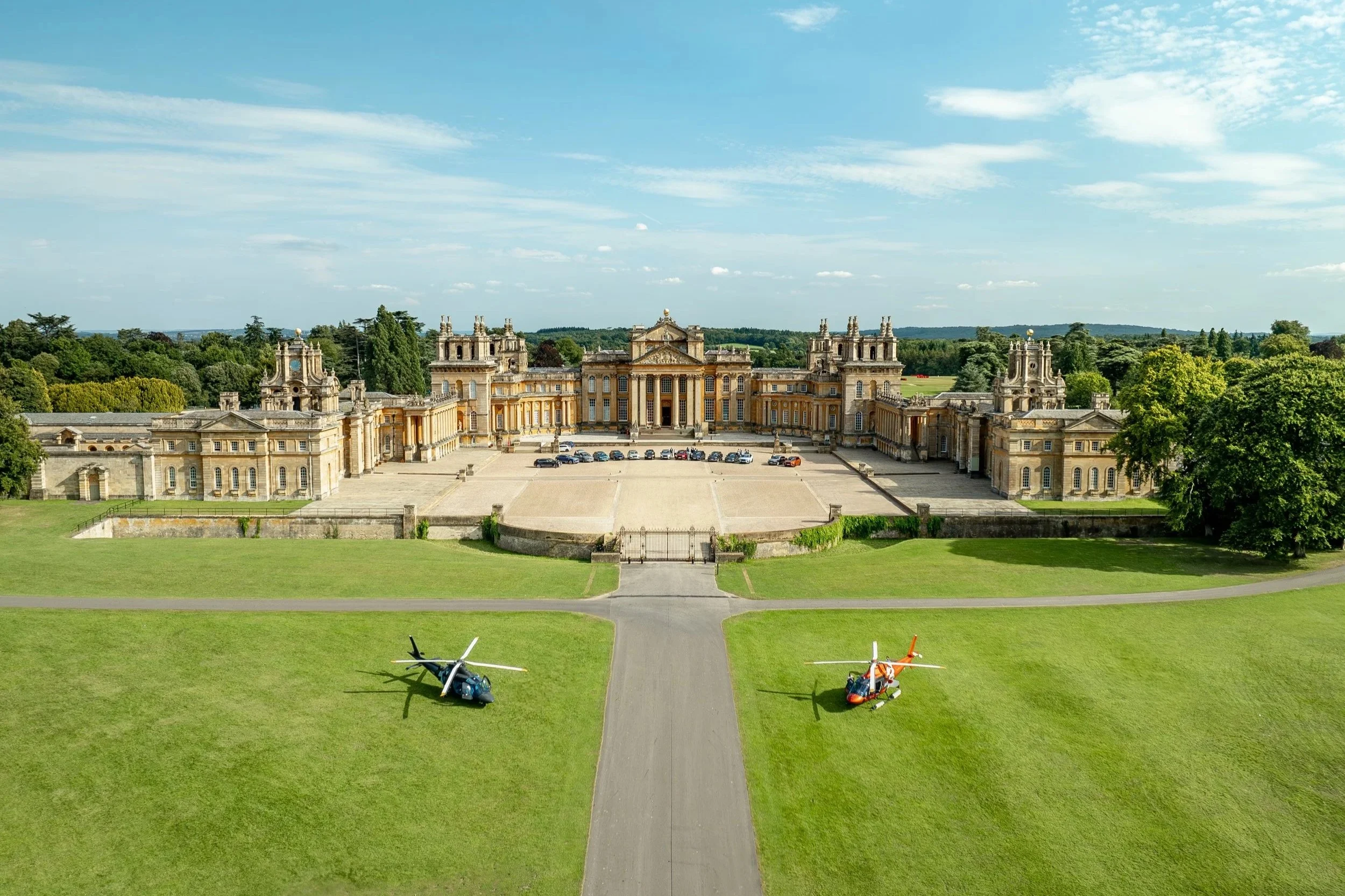 Aerial view of Blenheim Palace with two helicopters on a green lawn in front.