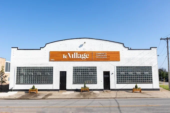 A white commercial building with a sign that reads 'Le Village' and mentions community coworking and childcare services, located in Lyons, IL