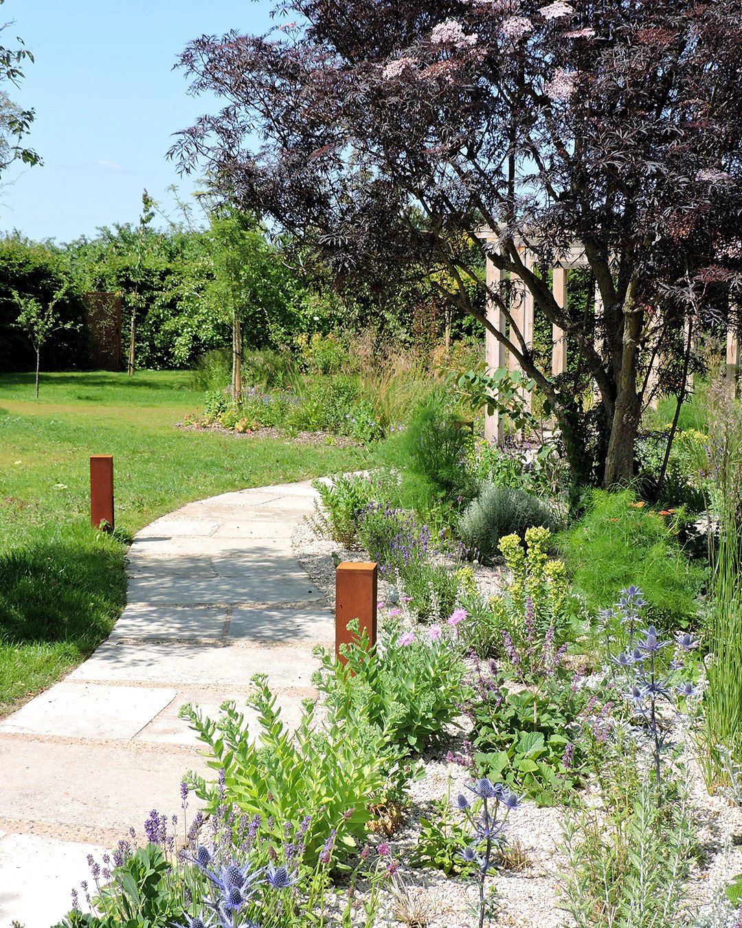 Summer shots of a lovely Norfolk garden we completed this year.⁠
⁠
The winding path takes you along the garden from the cobbled patio to the vegetable garden and is made from slabs repurposed from the previous patio.  To make the curves work we added