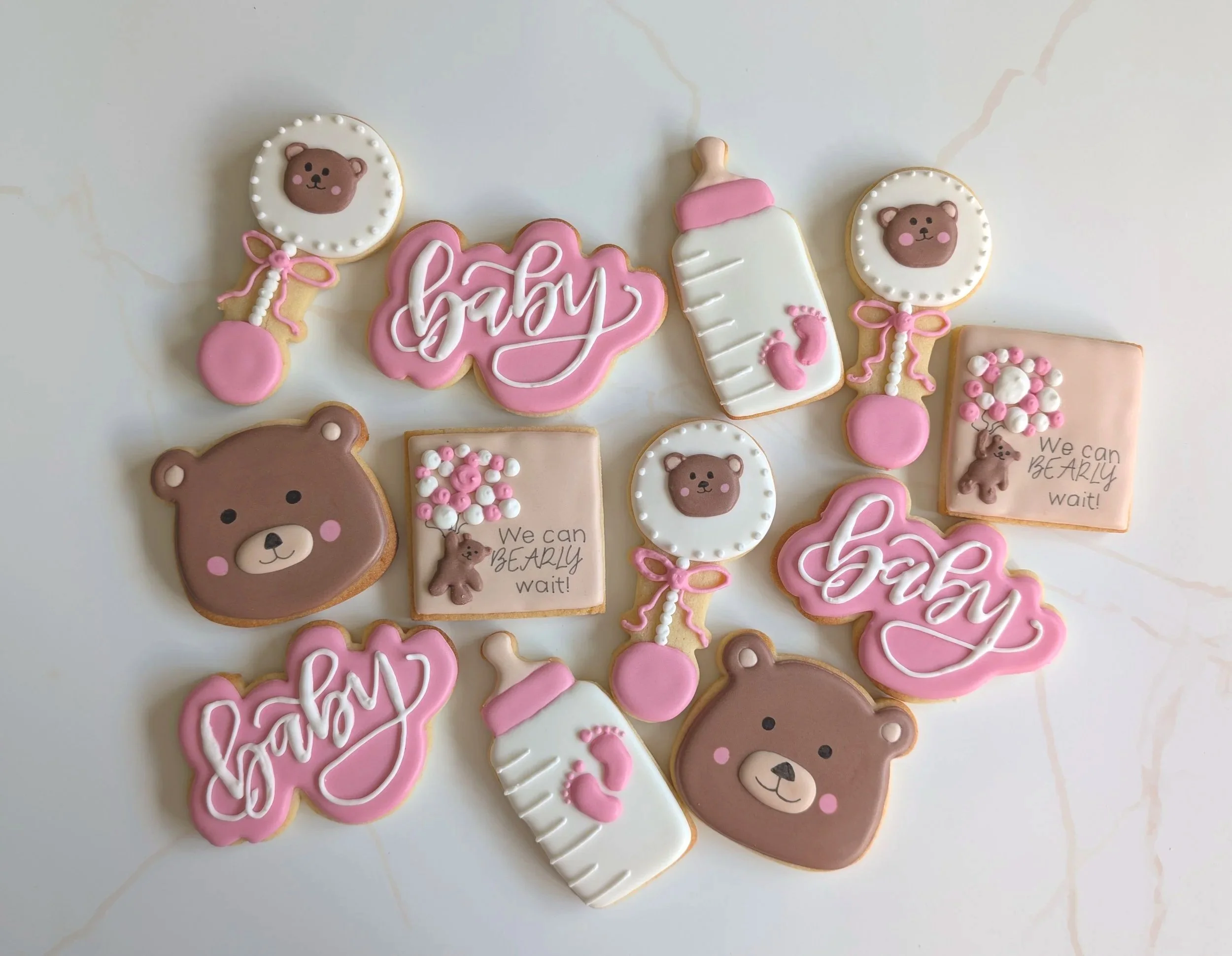 Decorative baby shower cookies with teddy bear faces, baby bottles, pink bows, and signs with 'baby' and 'We can BARELY wait' messages.