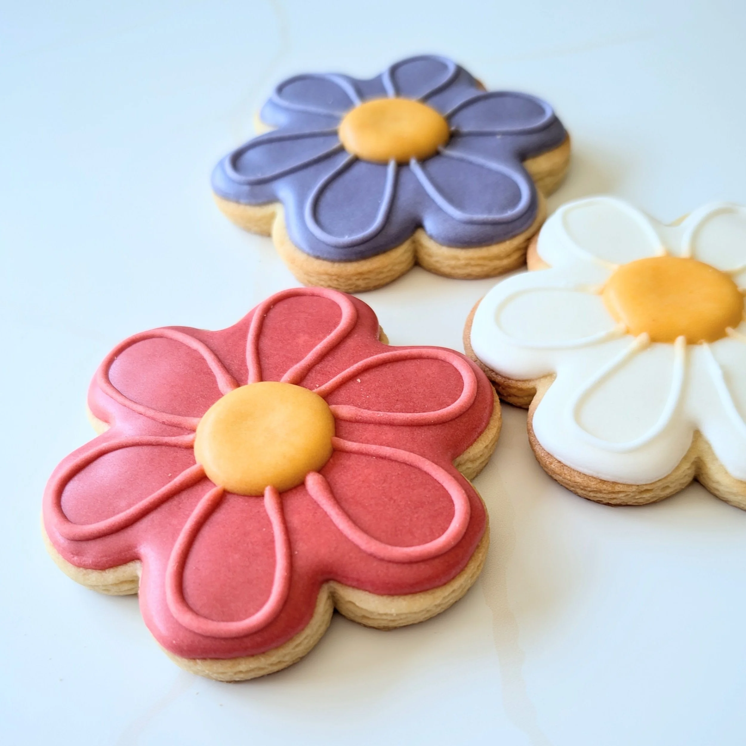 Decorative flower-shaped cookies with colorful frosting in pink, purple, and white, each with a yellow center.