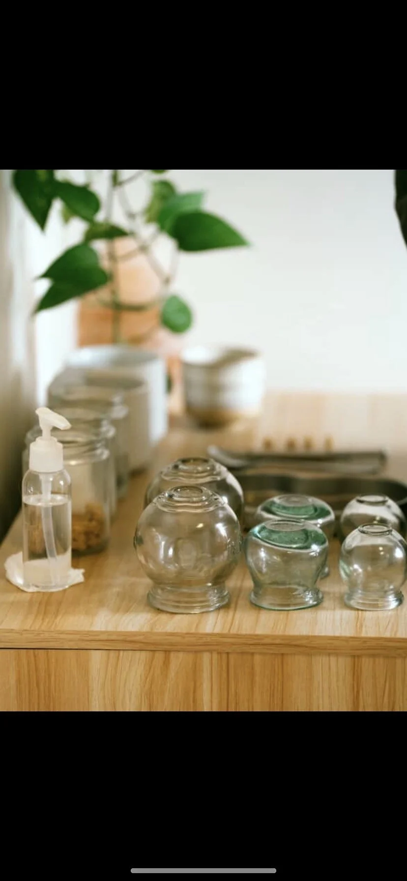 Glass cups upside down on a wooden surface, with a green plant and various kitchen containers in the background.