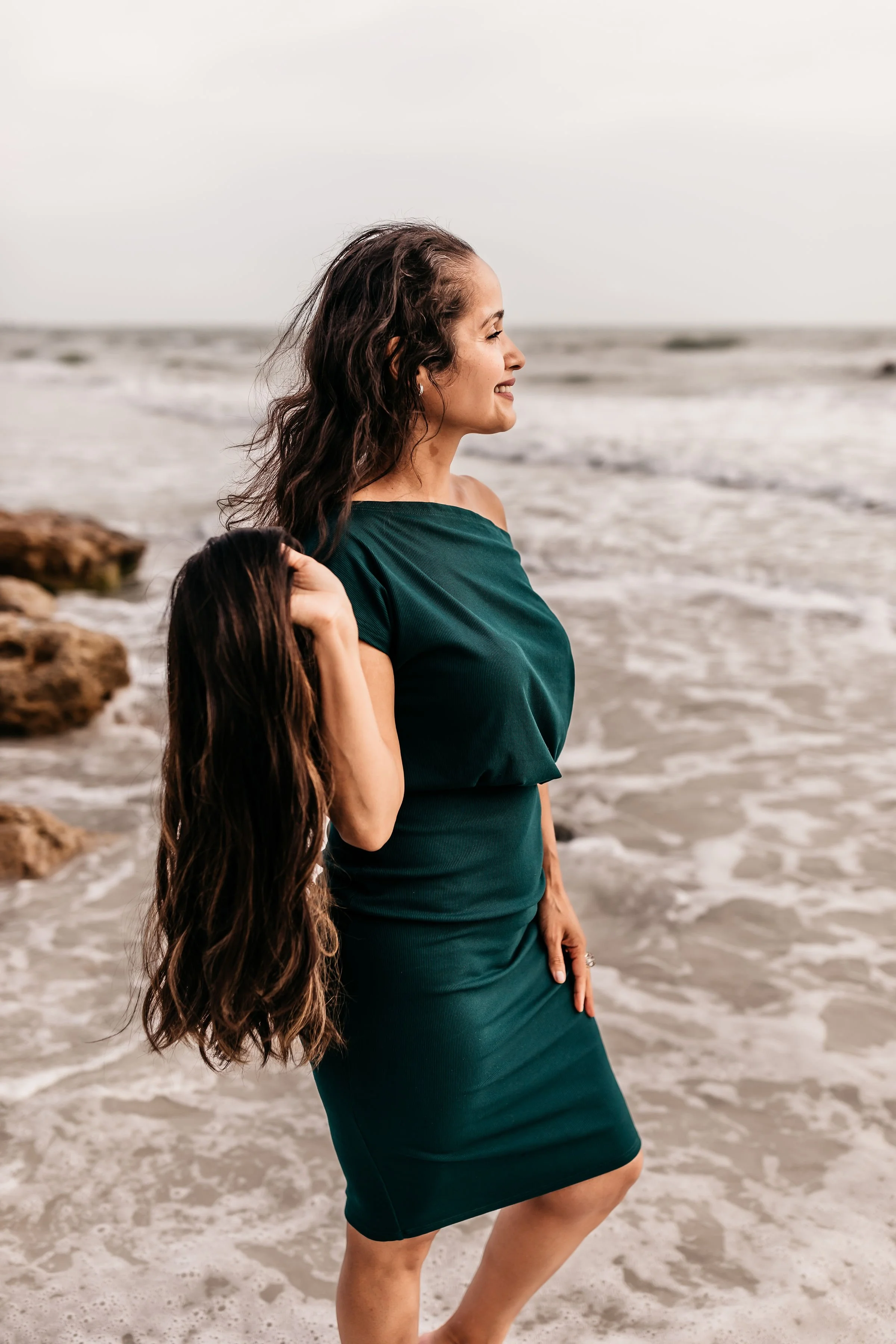 Profile pic of a woman with thinning hair holding her wig by the beach