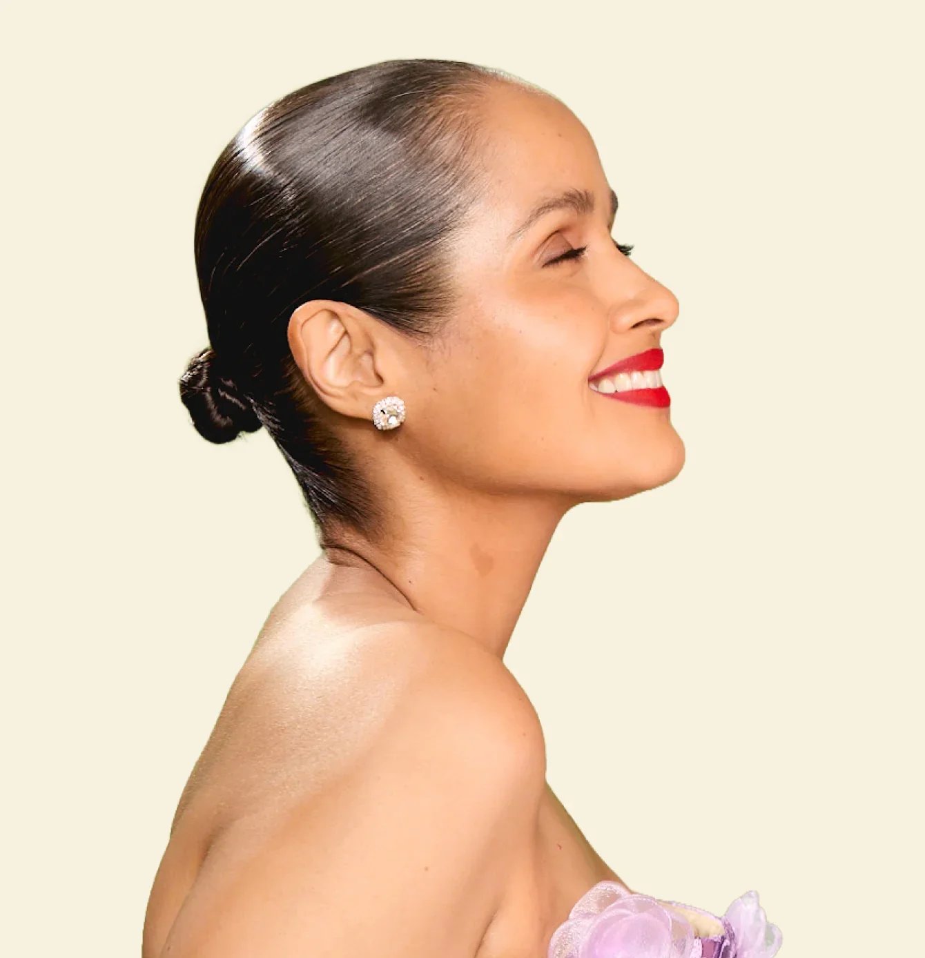 A woman with dark brown thinning hair pulled-back in a baby hair bun smiling with eyes closed, wearing red lipstick and diamond earrings, against a neutral background.